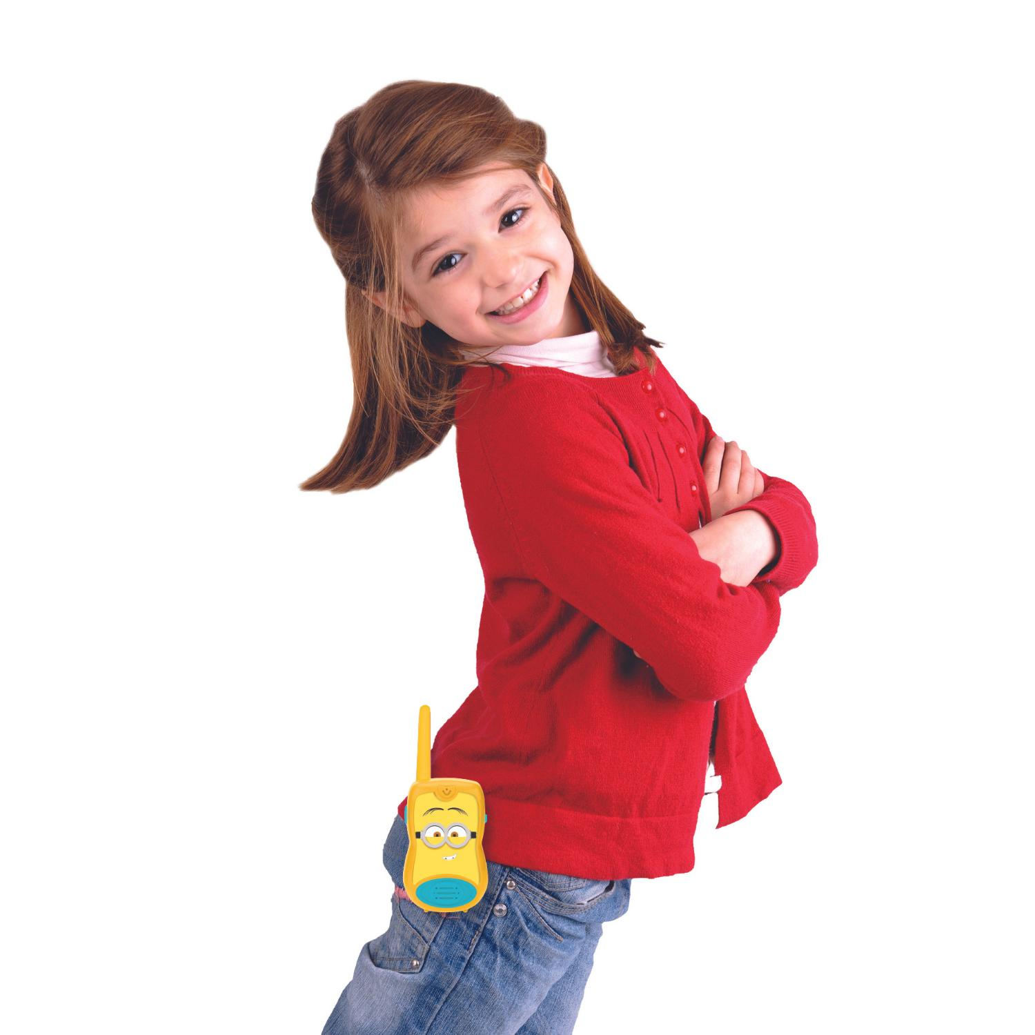 Une fille souriante avec un cardigan rouge et un jean, tenant un talkie-walkie Minions dans sa poche arrière.