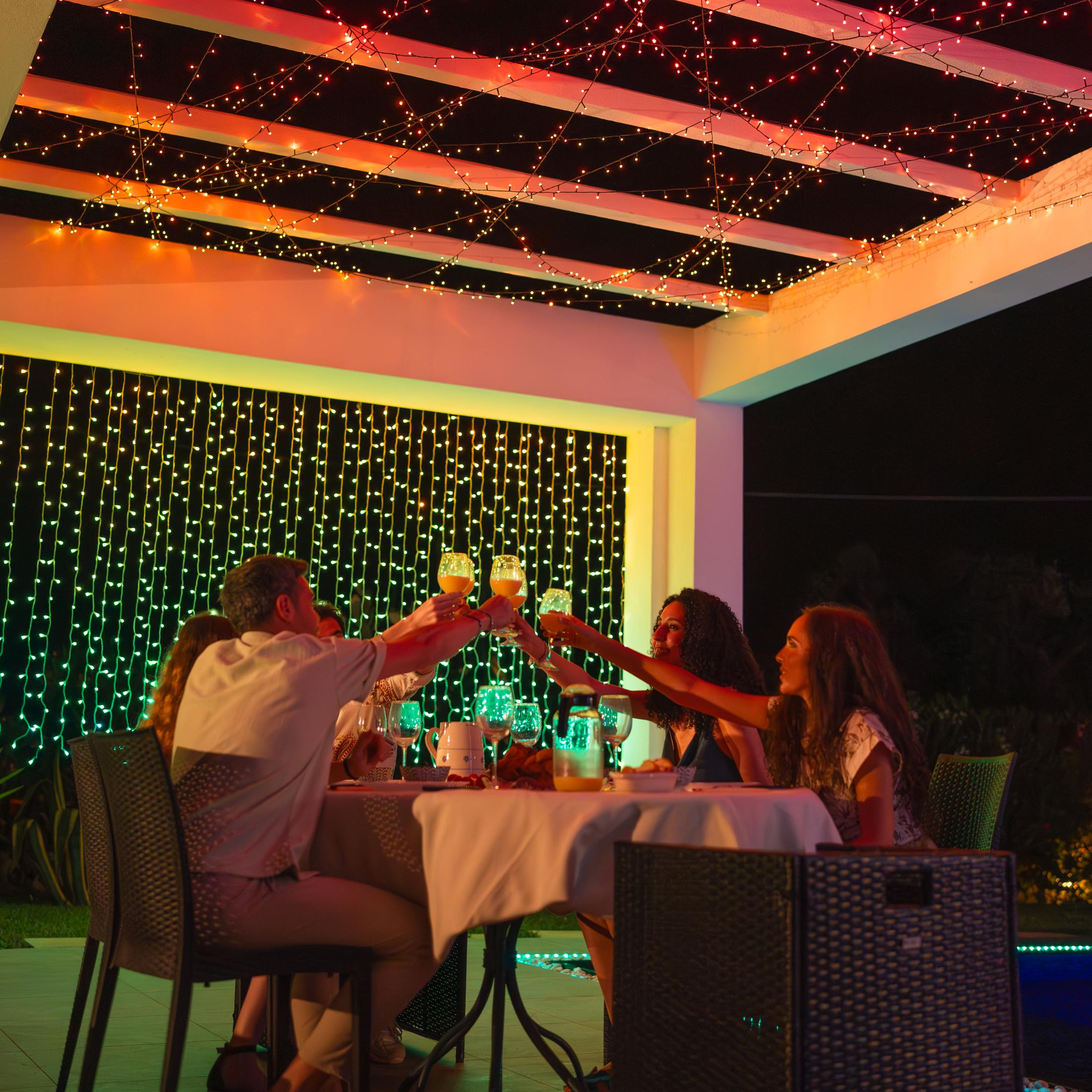 Ludzie wznoszący toasty napojami pod girlandami świetlnymi, tworząc świąteczną atmosferę w nocy.