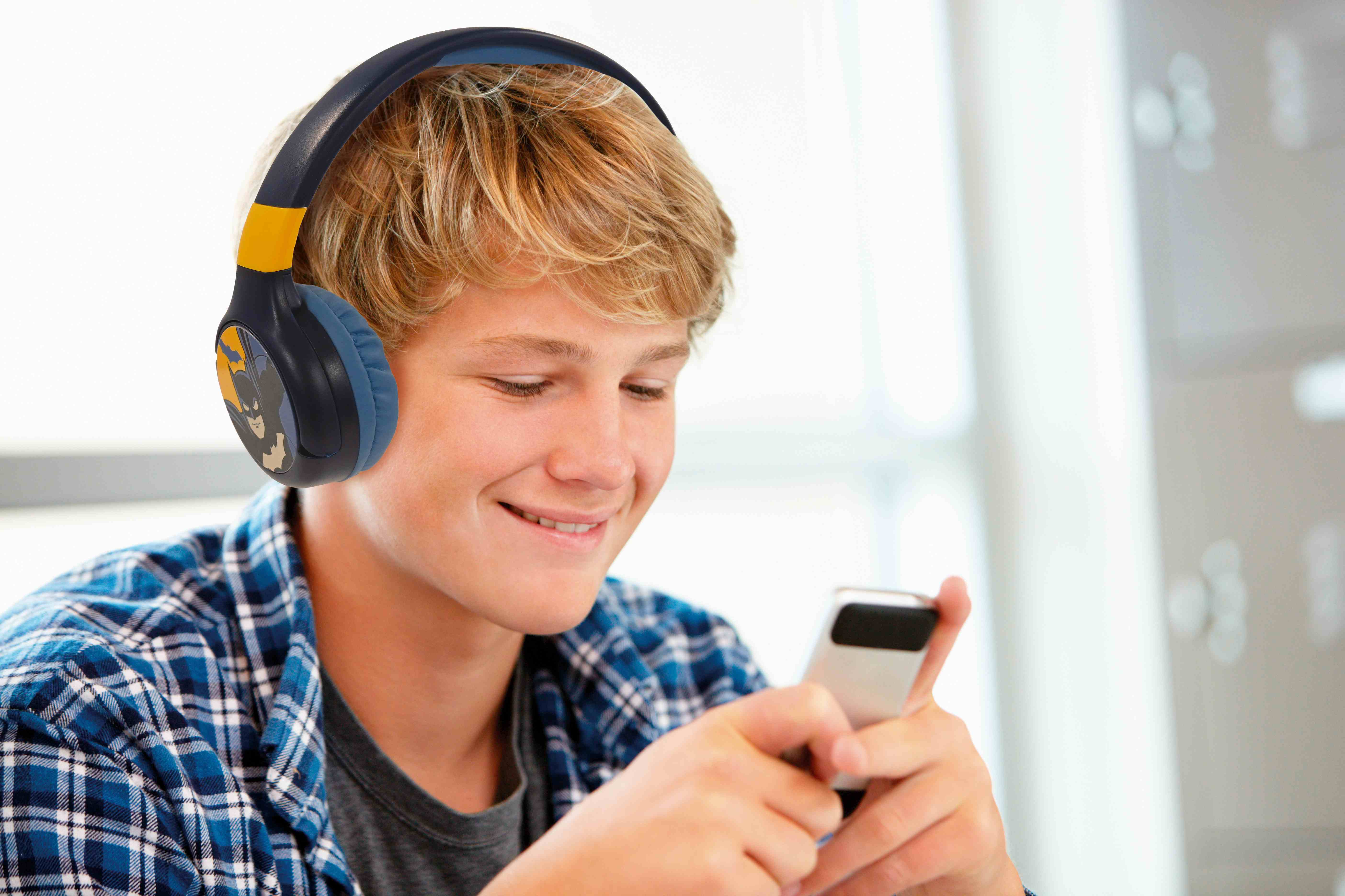 Ragazzo con cuffie, guarda uno smartphone. Sfondo: spazio ufficio sfocato.