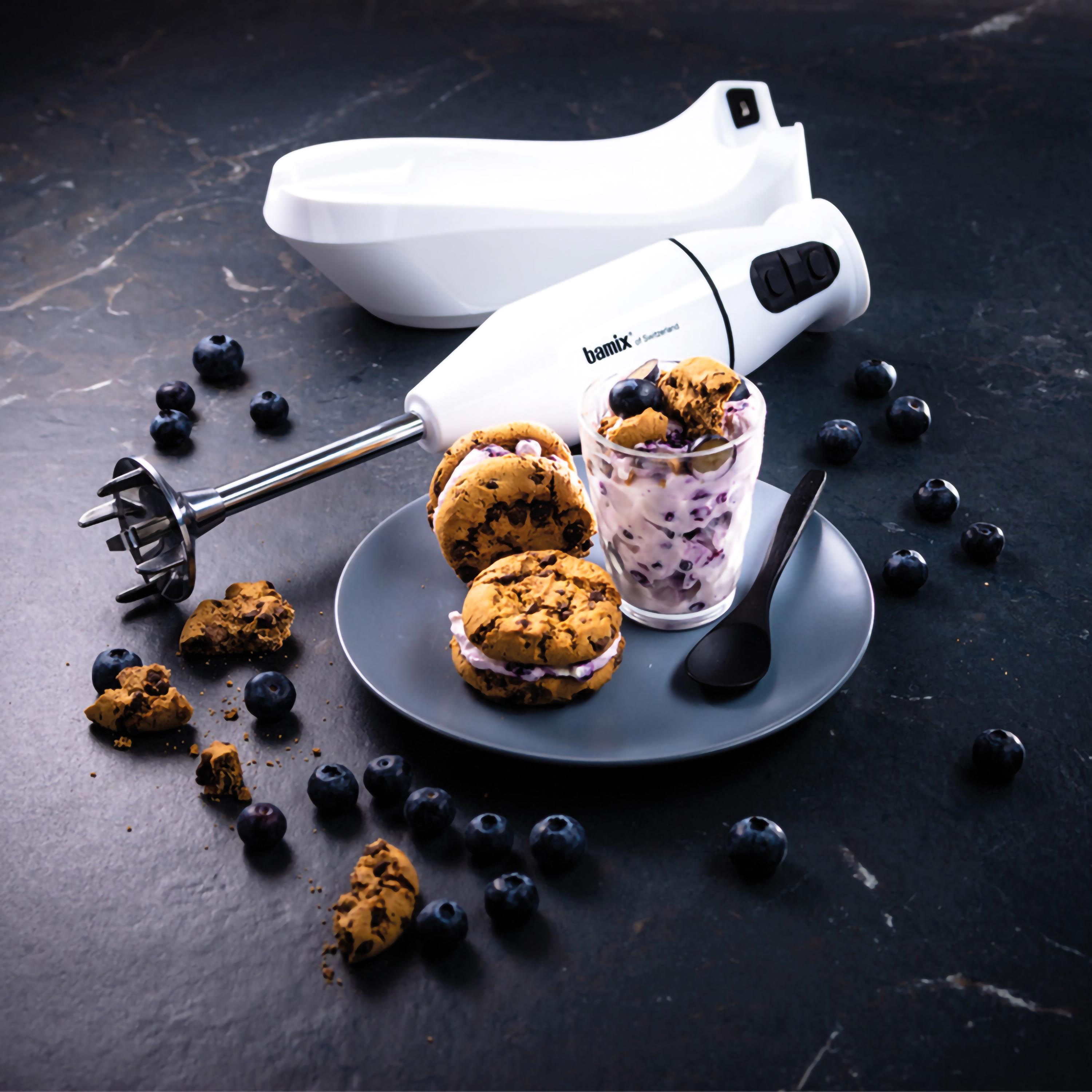 Un piatto con biscotti, mirtilli e una bevanda con mirtilli, con un frullatore a immersione bianco.