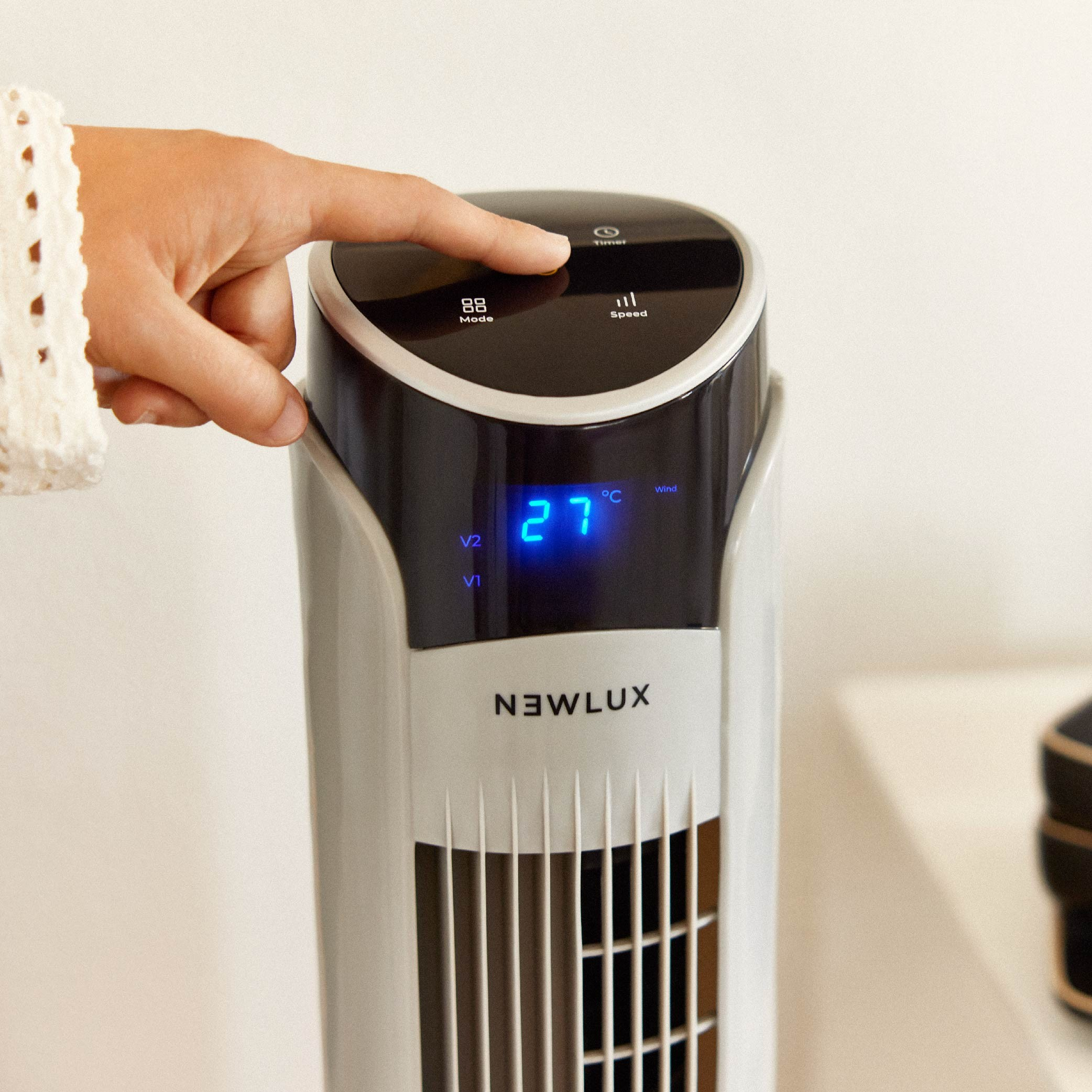 Una mano tocando un ventilador de torre con una pantalla digital que muestra 27 grados y botones.