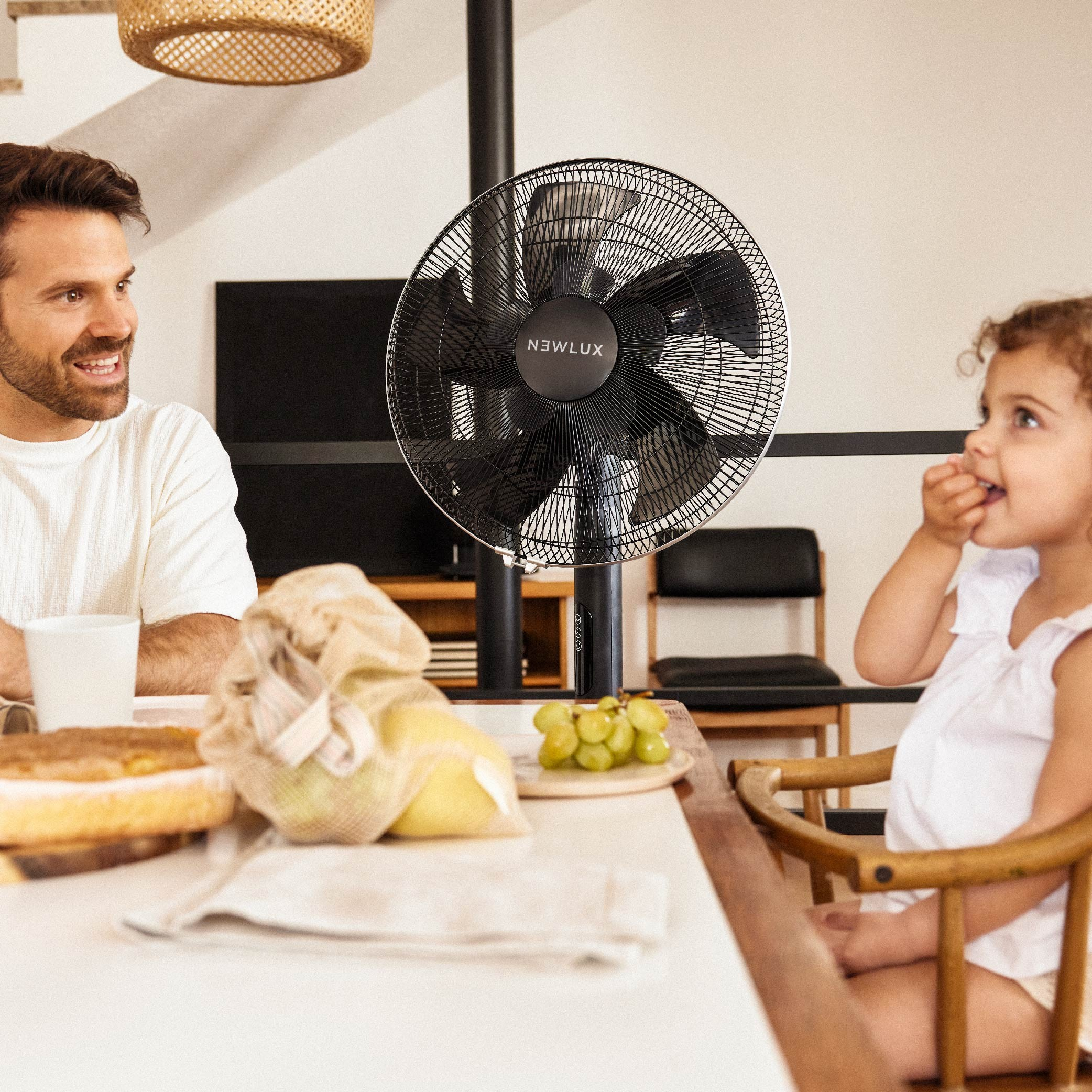 Un hombre y un niño en una mesa con un ventilador. Una mesa con comida y frutas.