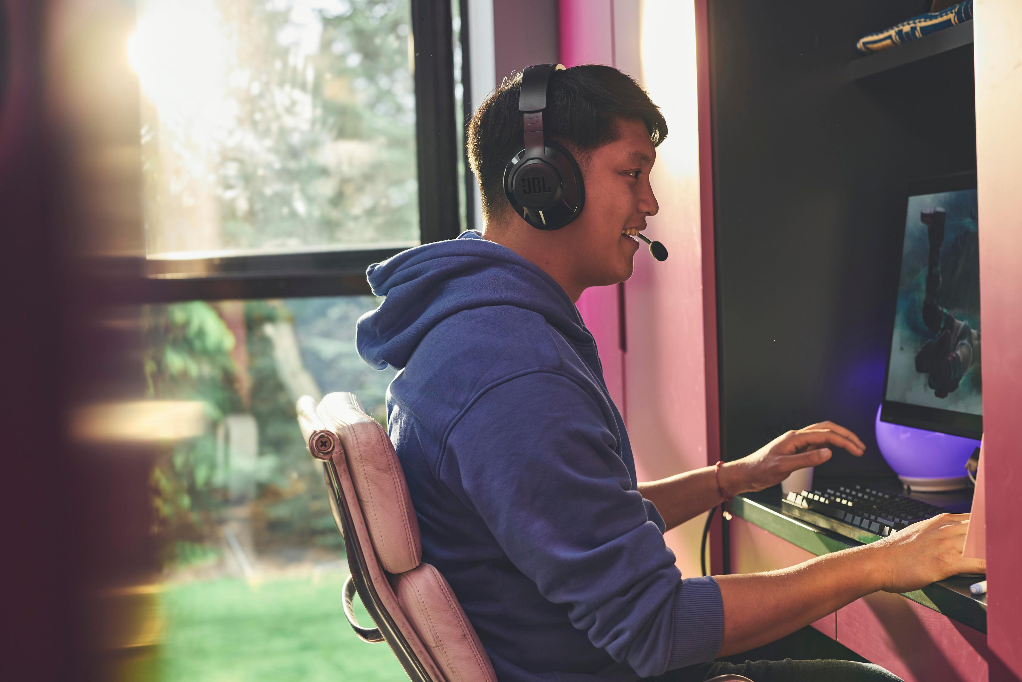 Mężczyzna w słuchawkach gra na komputerze. Uśmiechnięty i skupiony, w konfiguracji do gier.