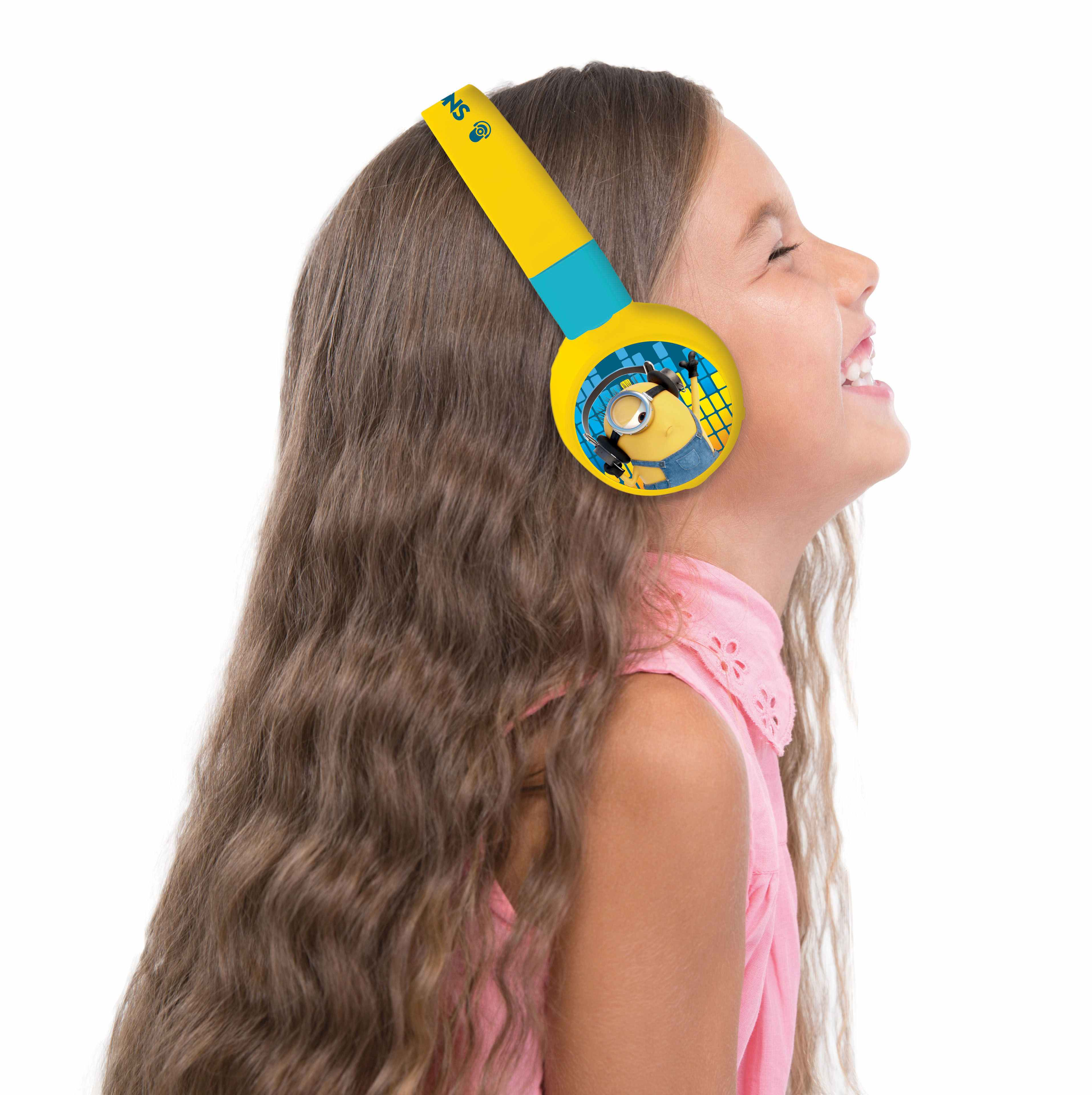 Bambina con cuffie gialle dei Minions, che ride, su sfondo bianco.