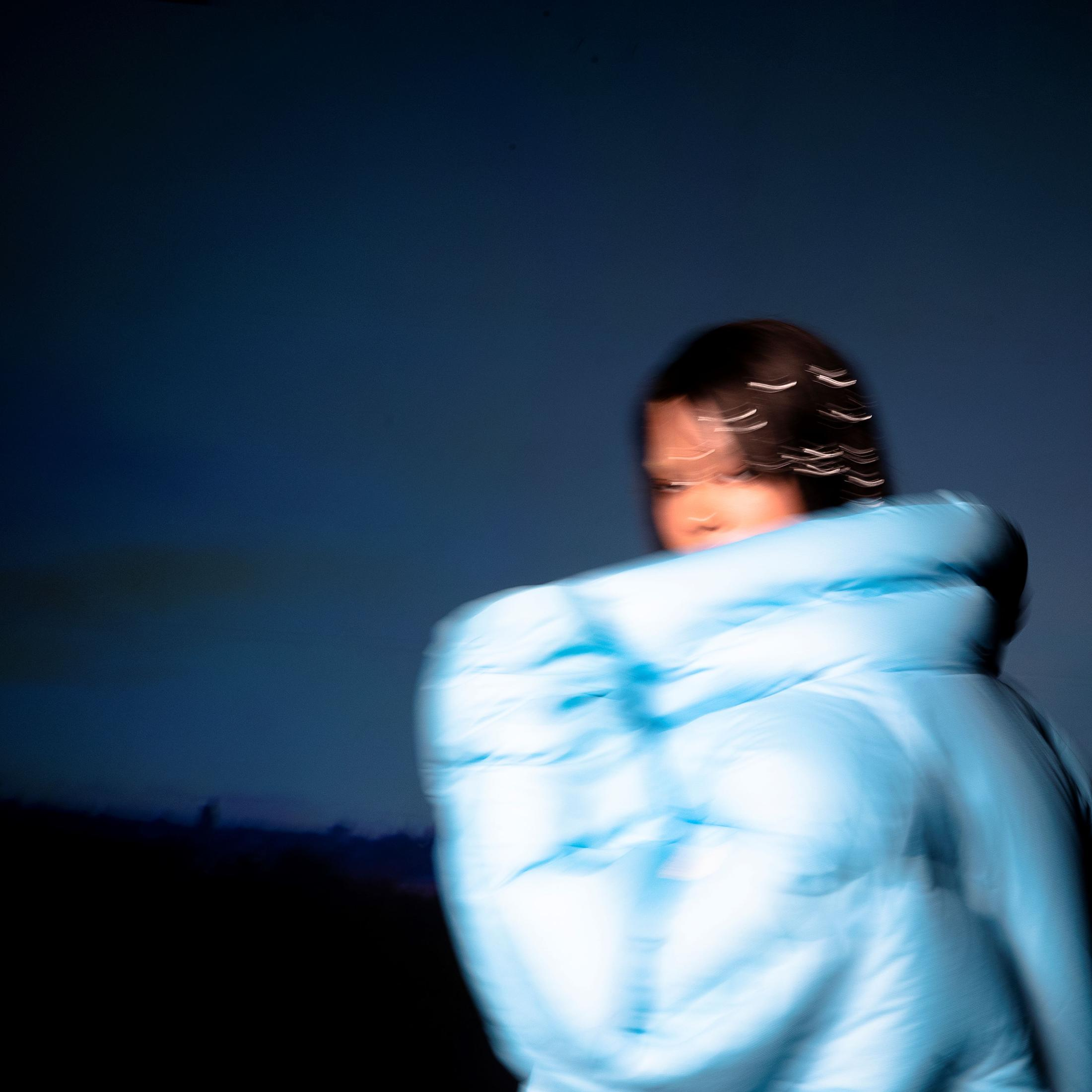 Abstracte afbeelding van een persoon in een blauwe jas, vaag tegen een donkerblauwe achtergrond.