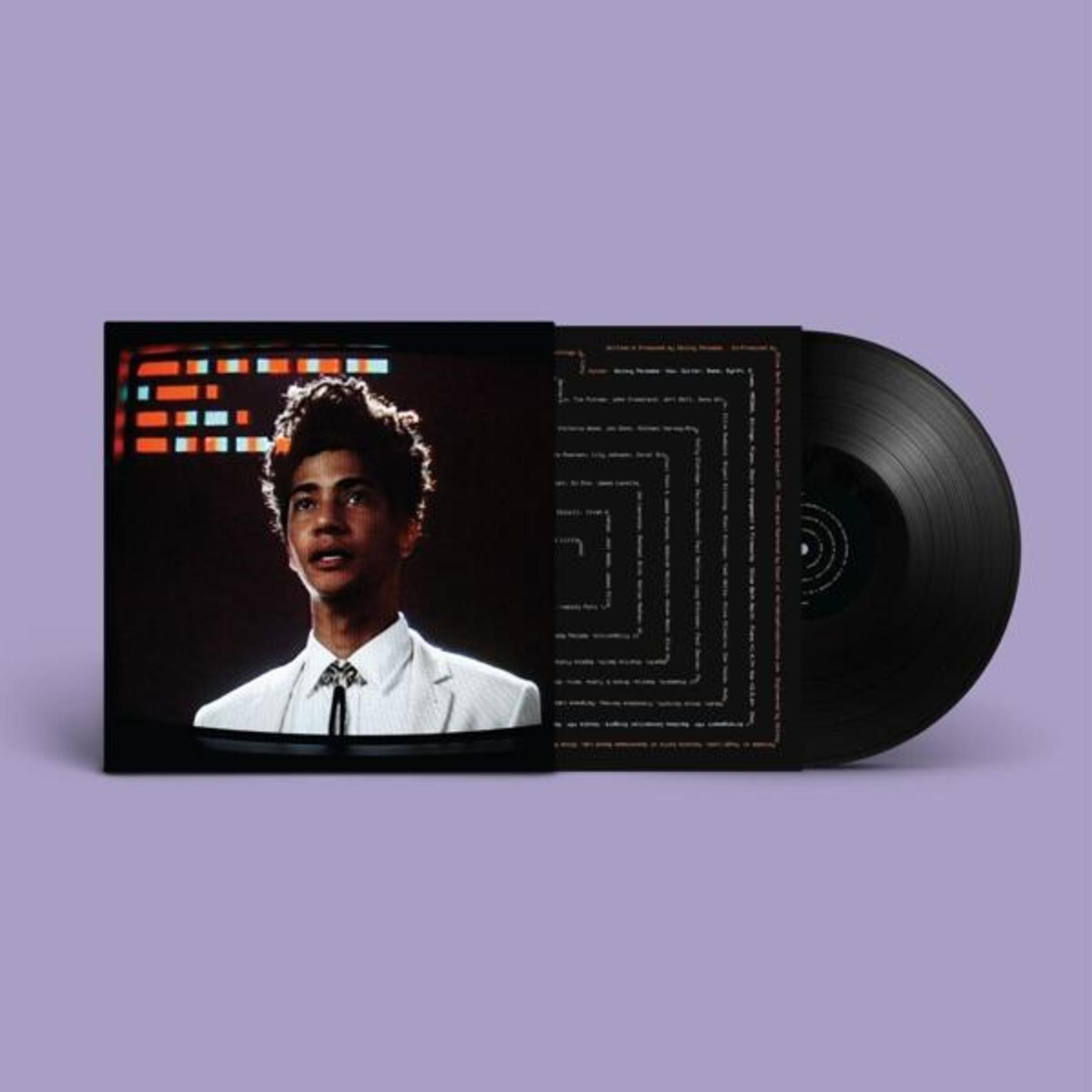 Copertina dell'album in vinile. Un giovane in giacca e cravatta guarda in alto davanti a uno schermo con luci arancioni.
