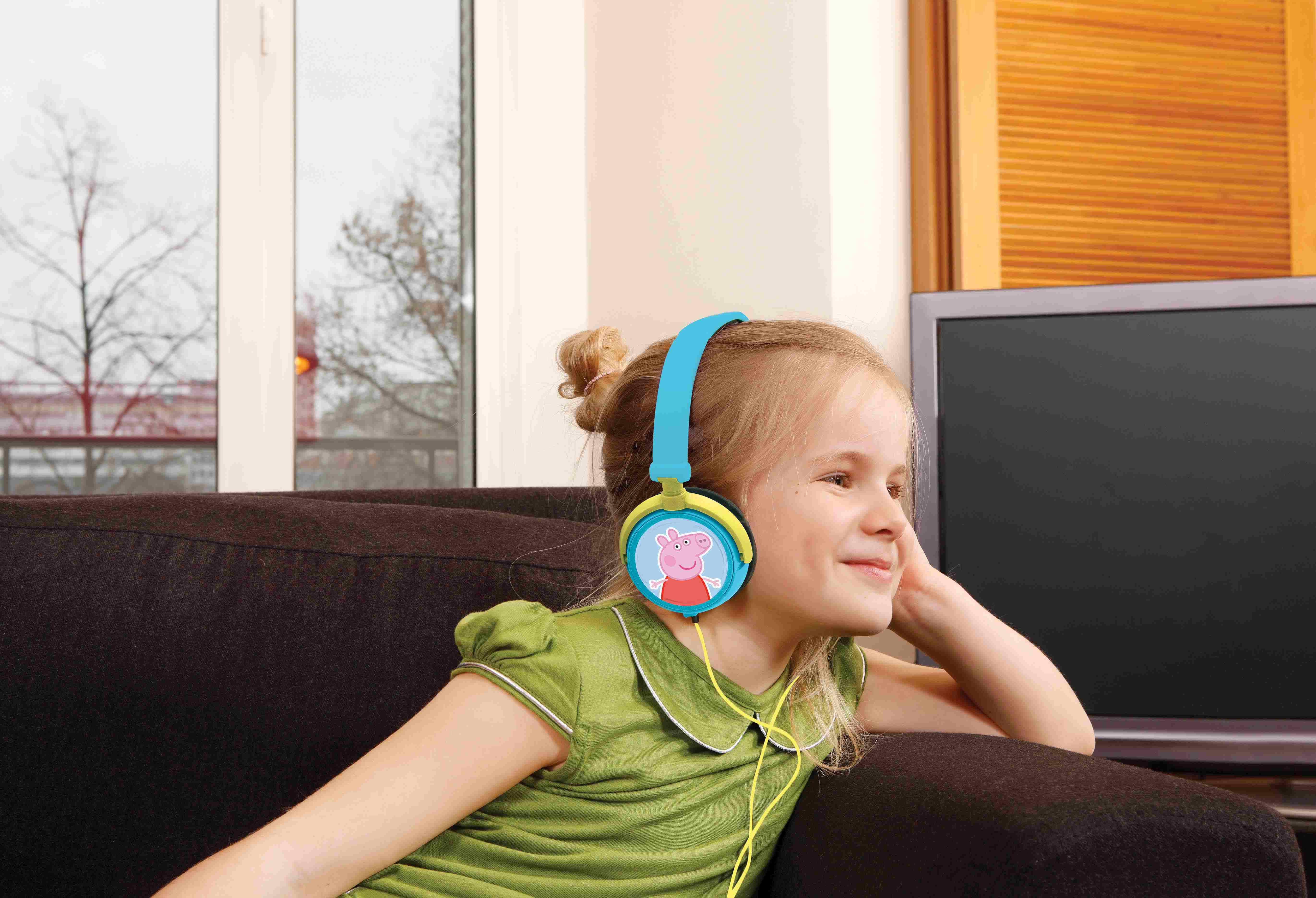 Una bambina con cuffie di Peppa Pig, sorridente. Seduta su un divano, guarda di lato.