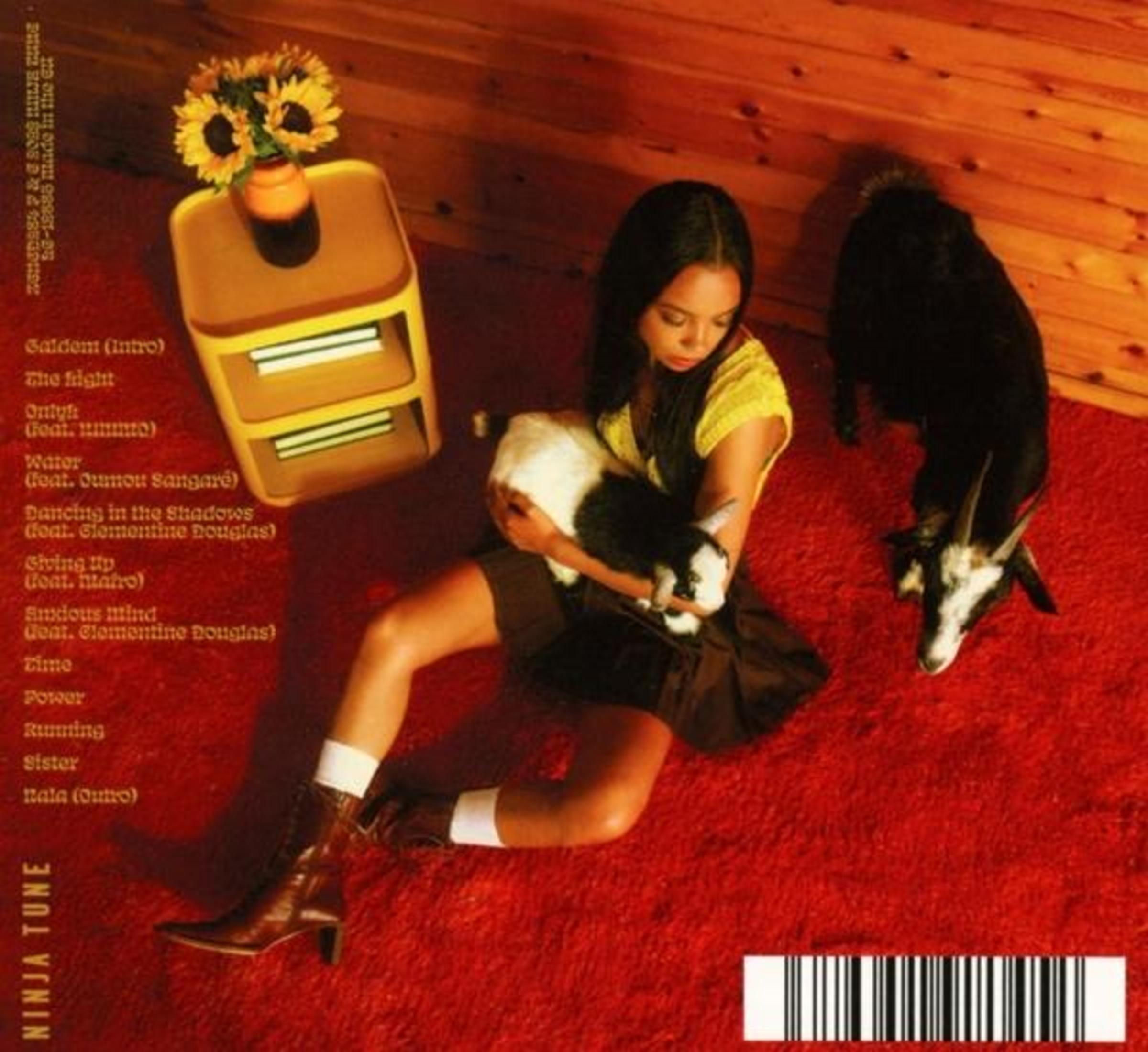 Copertina dell'album con una donna che tiene una capra. Un girasole e un tappeto rosso sono nella scena.