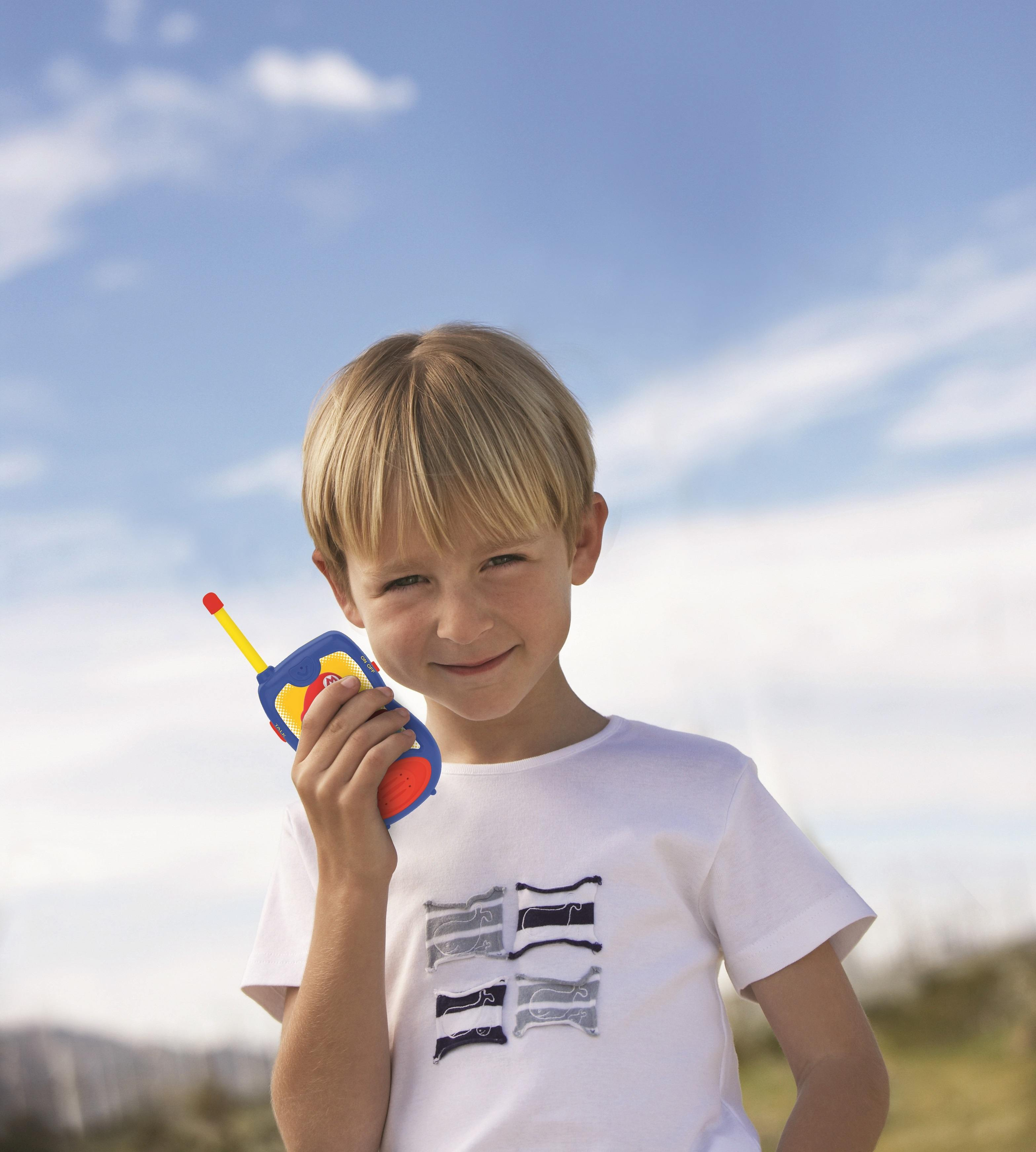 Niño con un walkie-talkie de Mario, sonriendo. Cielo azul. Camisa blanca.