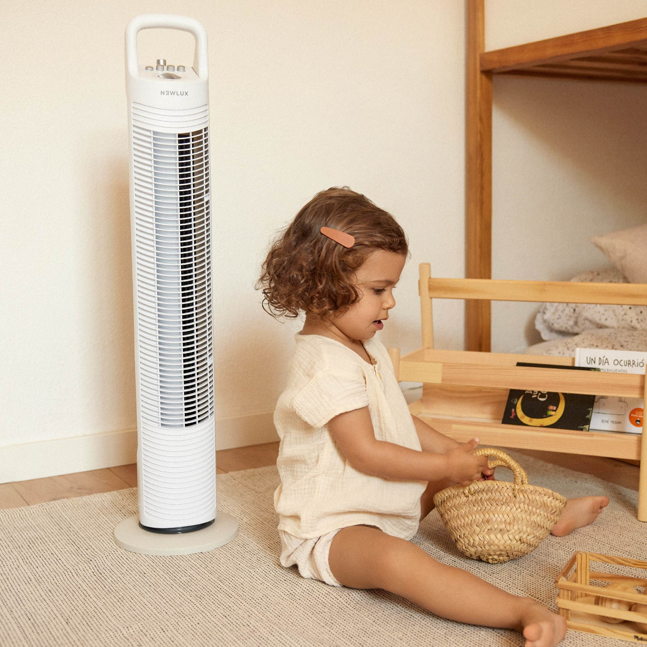 Una niña y un ventilador en una habitación. El ventilador es blanco, alto.
