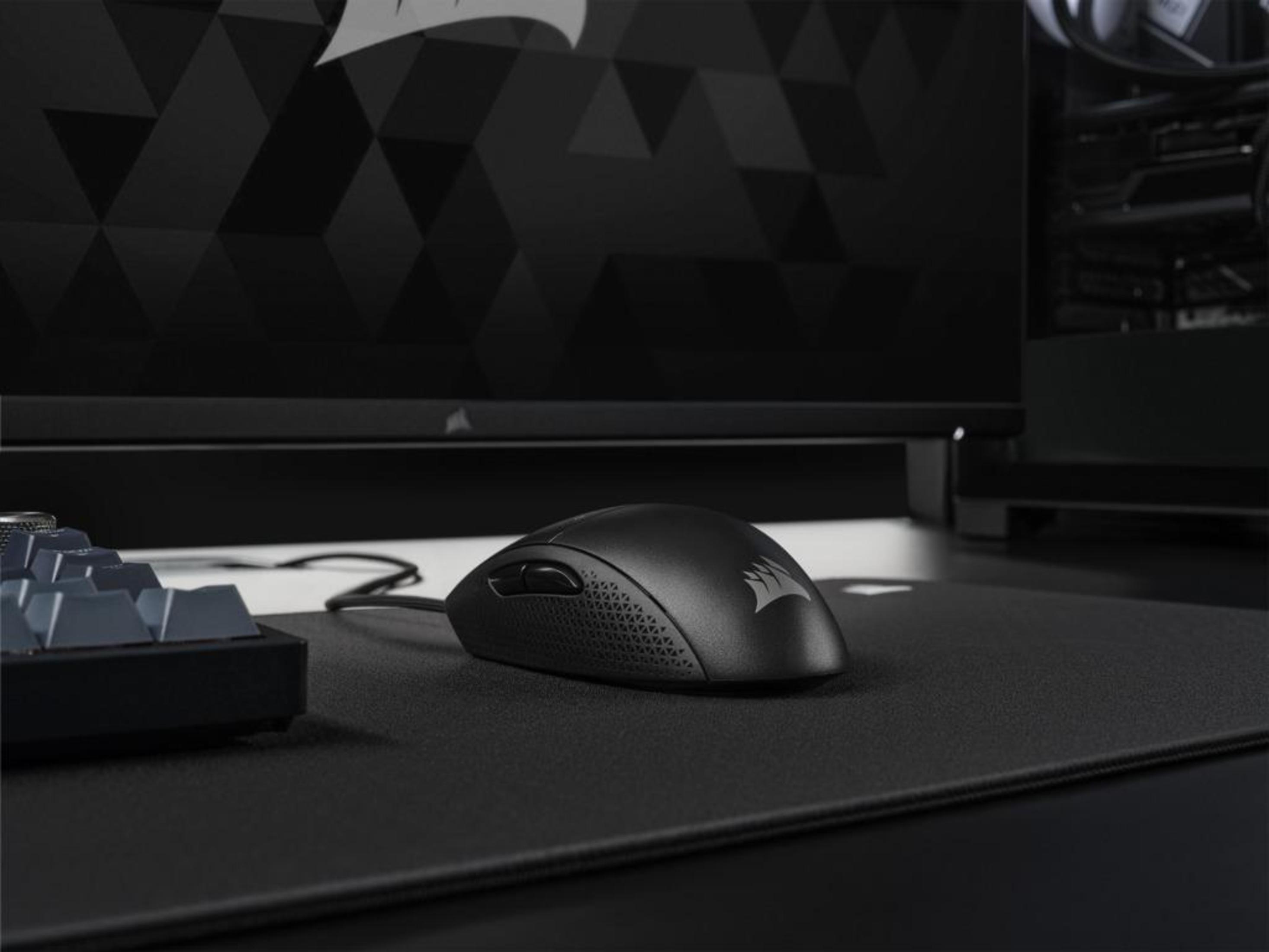 Czarna mysz gamingowa Corsair na czarnej podkładce, z monitorem w tle.