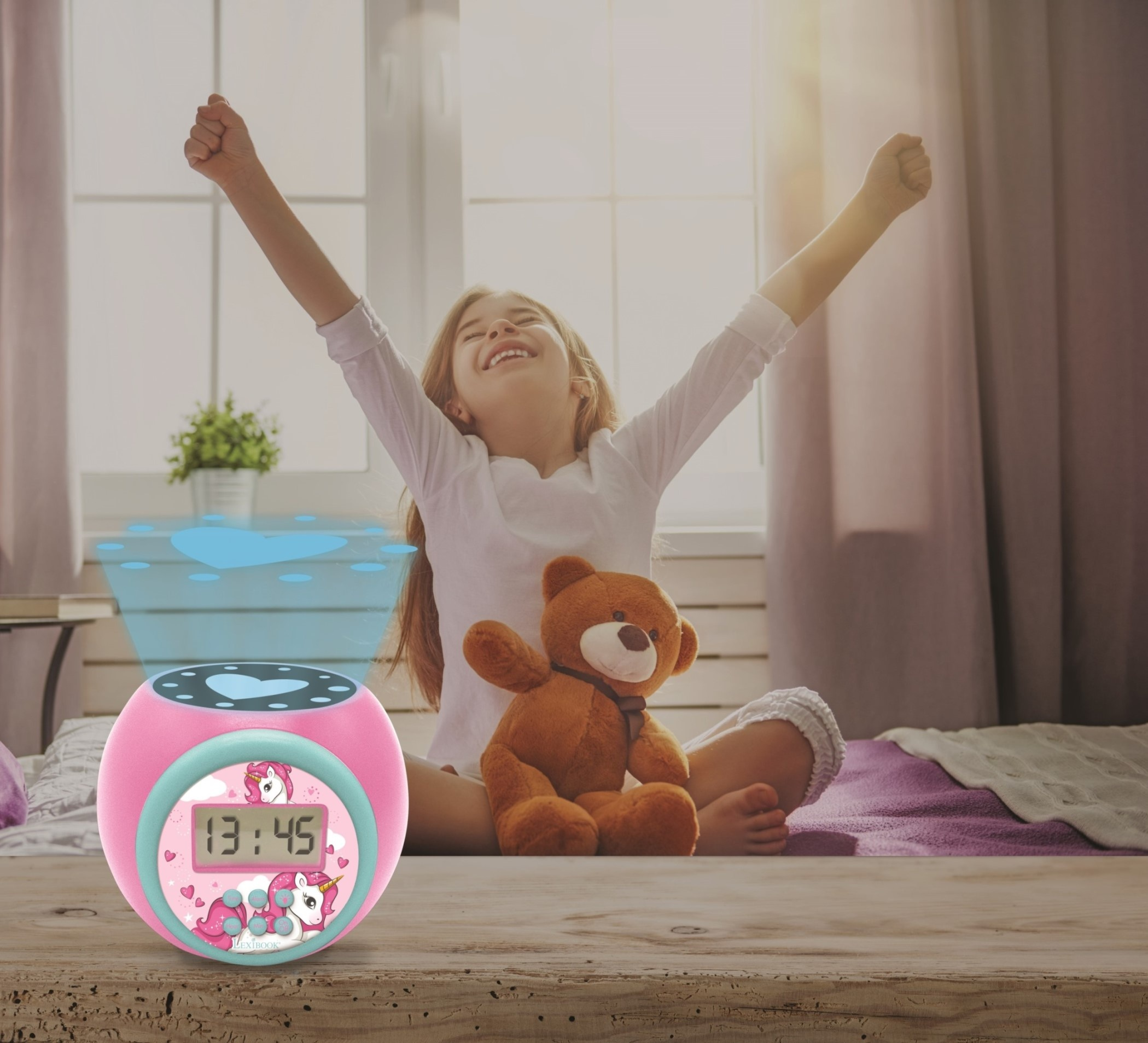 Una bambina sorride con le braccia alzate. Una sveglia rosa e un orsacchiotto sono vicini su un letto.