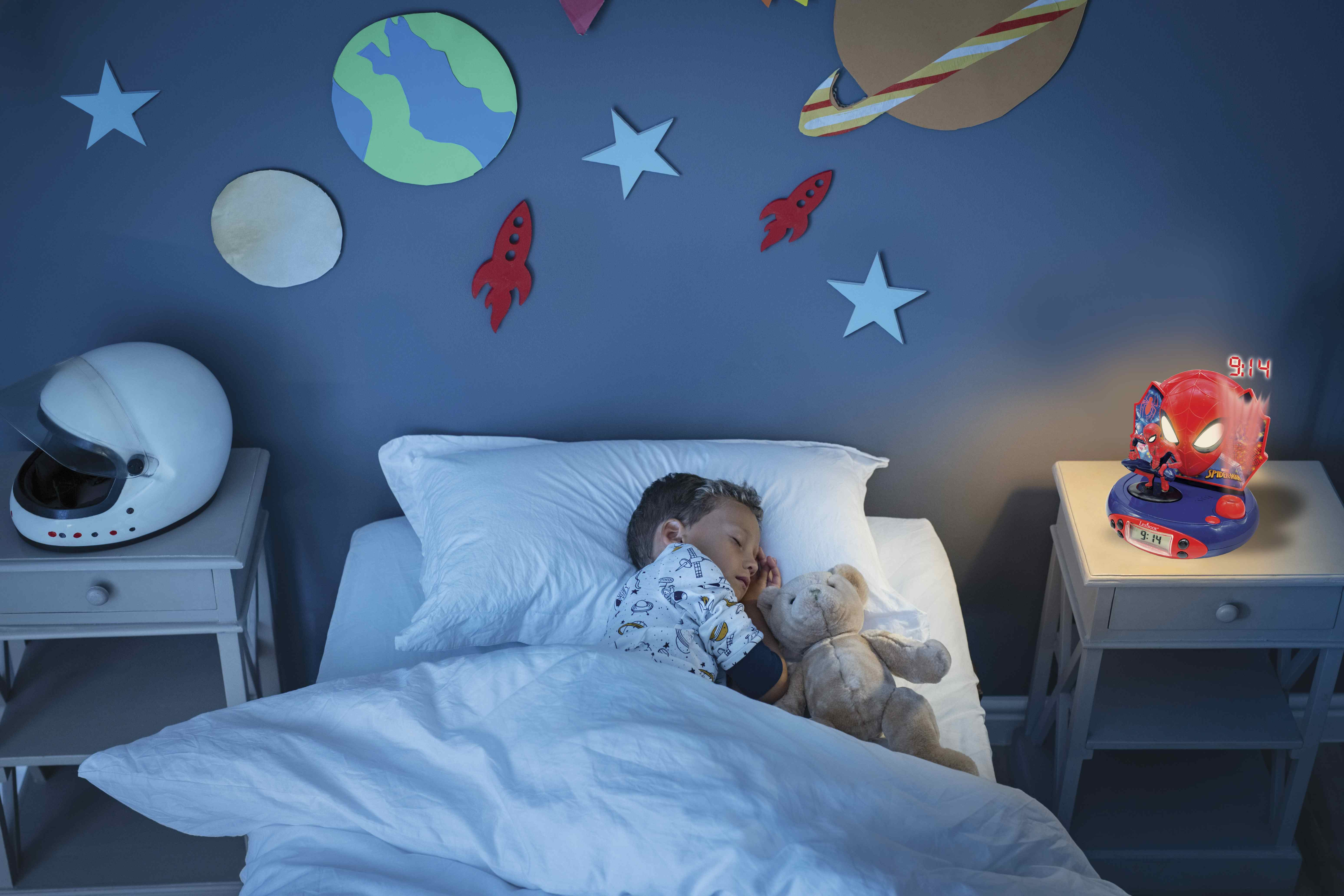 Un niño durmiendo con un despertador de Spider-Man. Una mesita de noche con un casco junto a la cama.