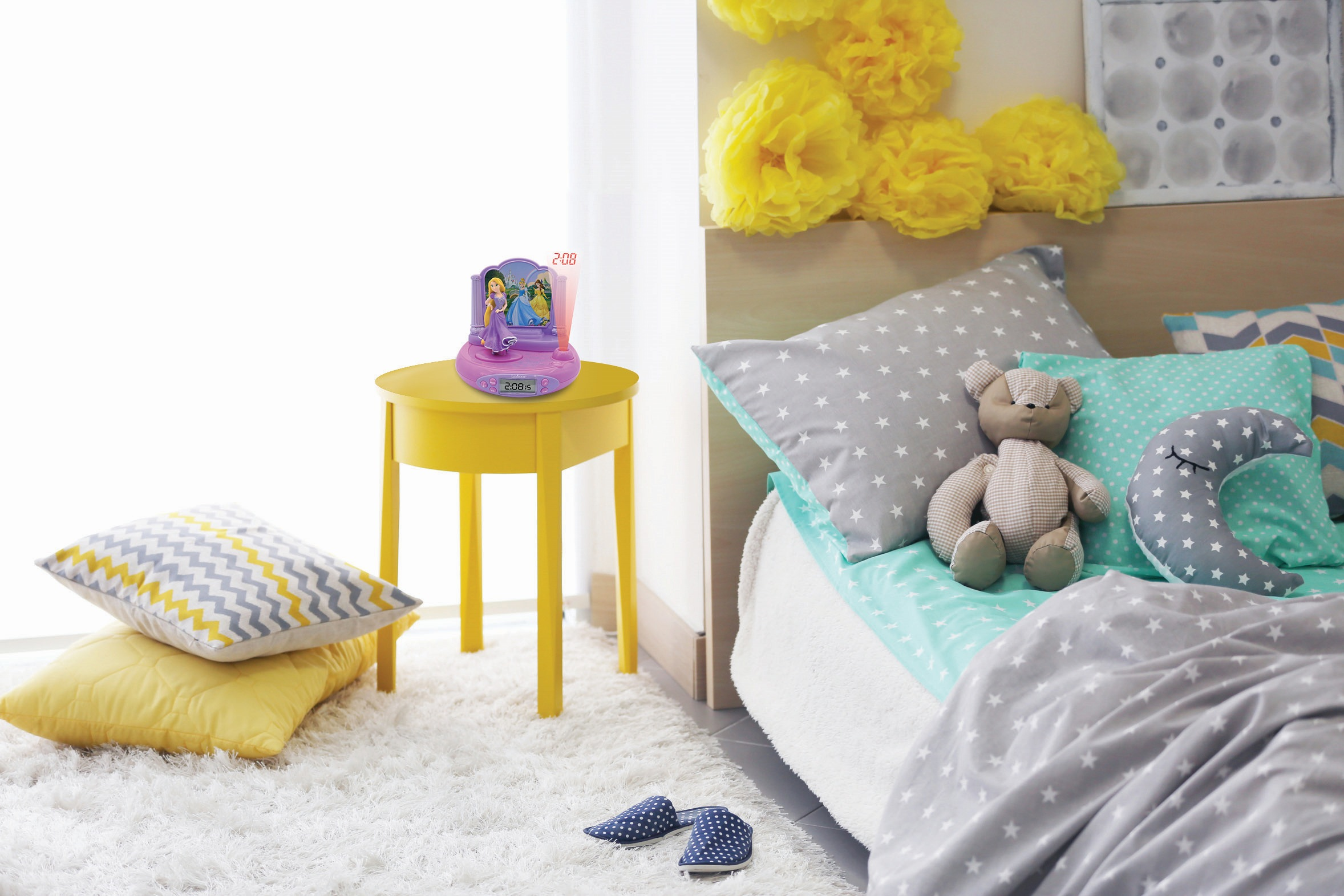 Un dormitorio infantil con una mesa amarilla, cama y juguetes. Una lámpara con temática de princesas está en la mesa.