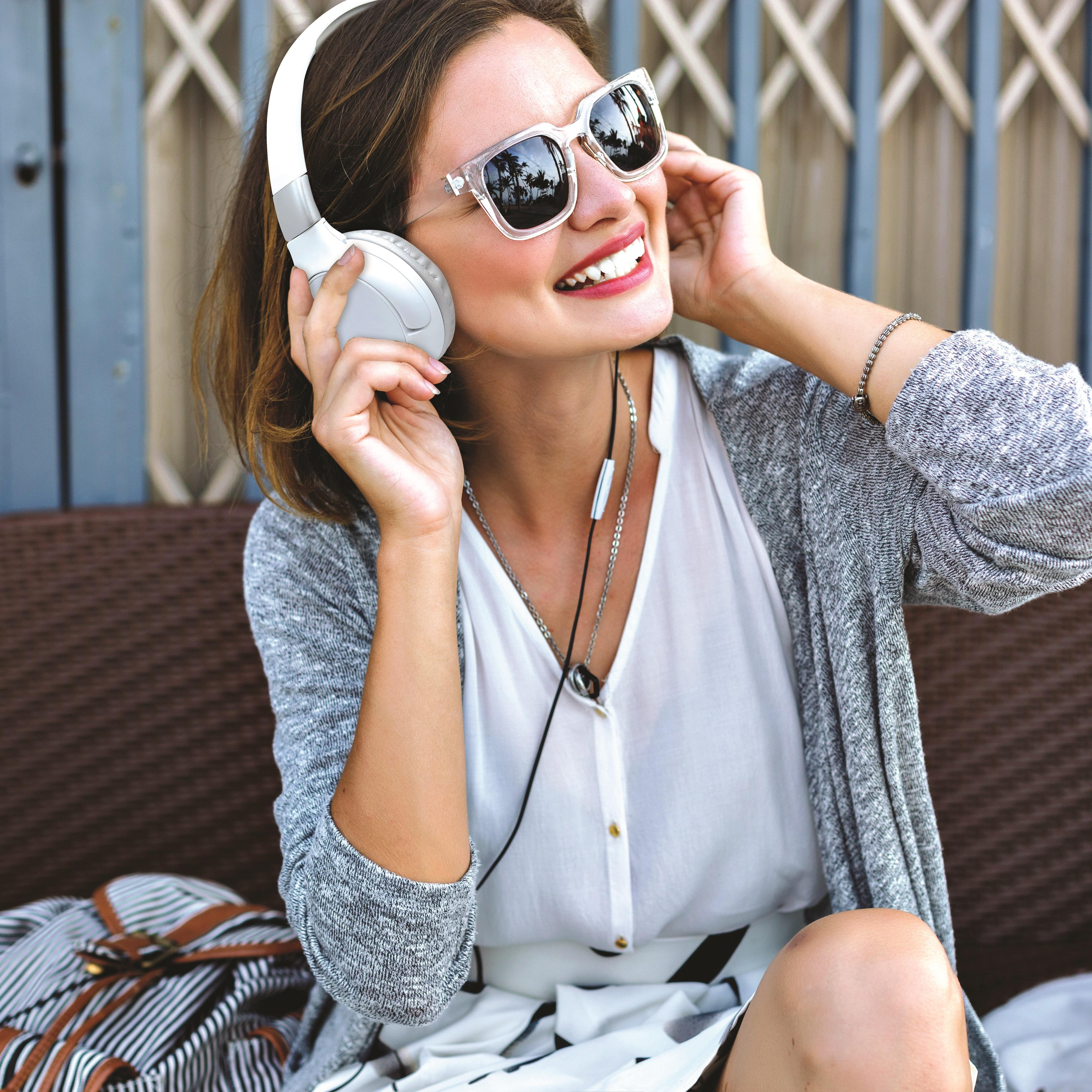 Frau mit Kopfhörern und Sonnenbrille lächelt beim Musik hören im Freien.