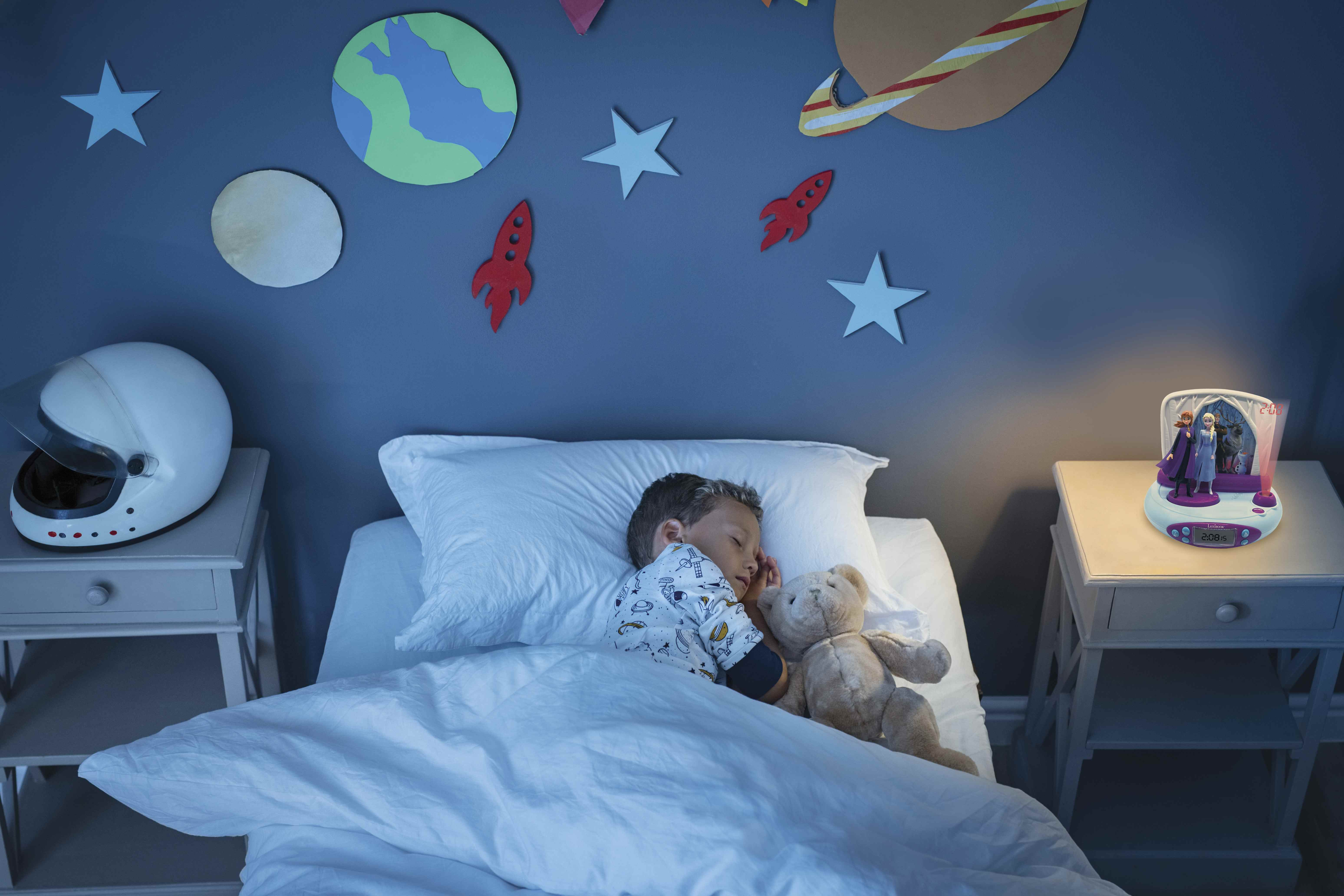 Un niño durmiendo en la cama con un despertador de Frozen y decoración espacial.