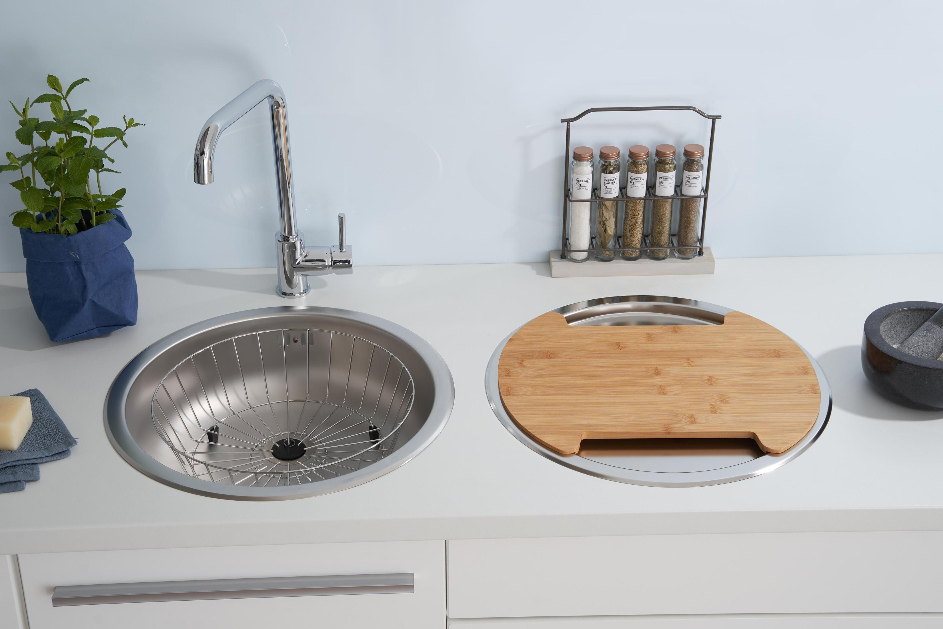 Küchenspüle mit Edelstahlbecken, Schneidebrett und Gewürzgläsern auf einer Arbeitsplatte.