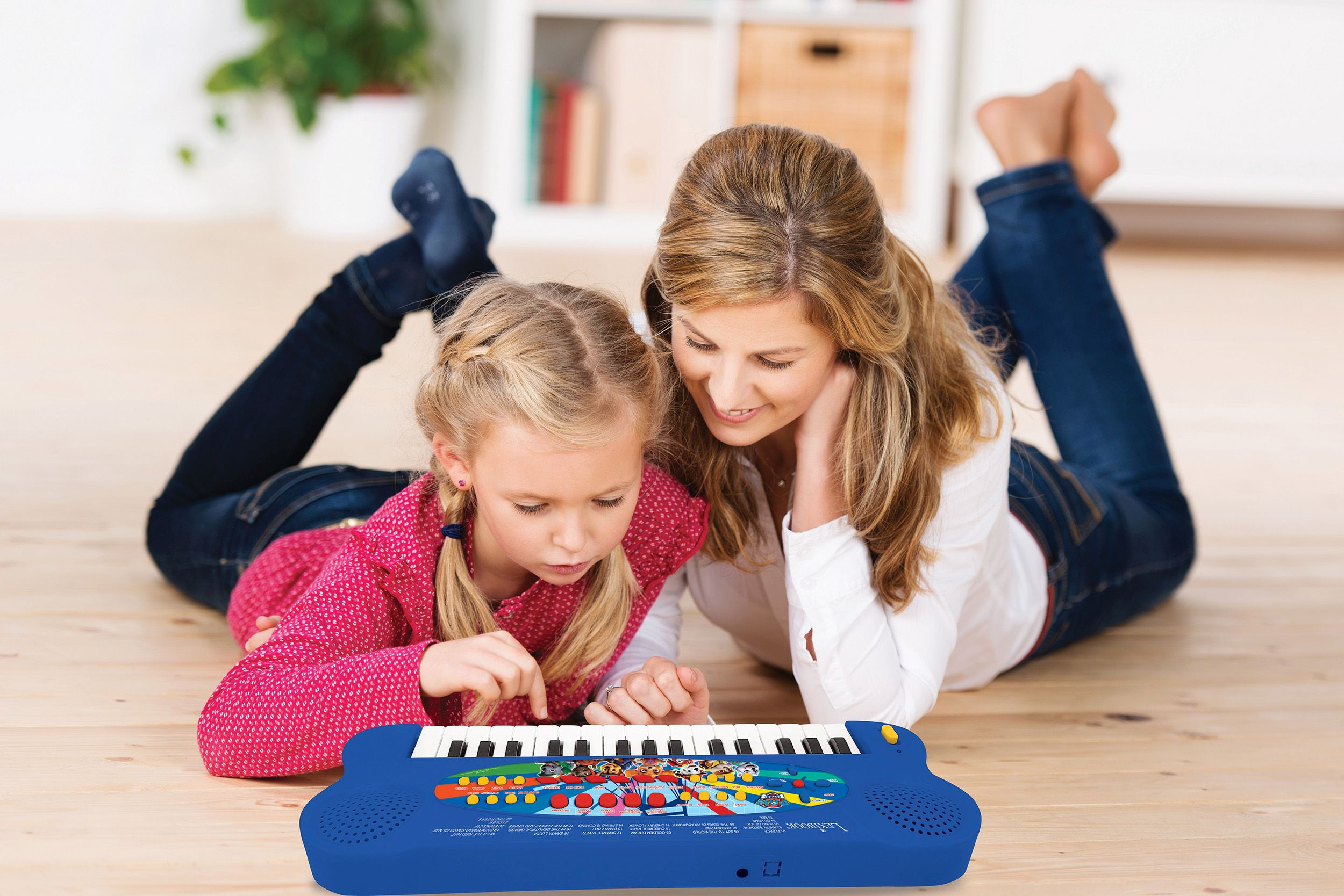 Mutter und Tochter spielen zusammen auf einem Holzboden ein Spielzeugklavier.