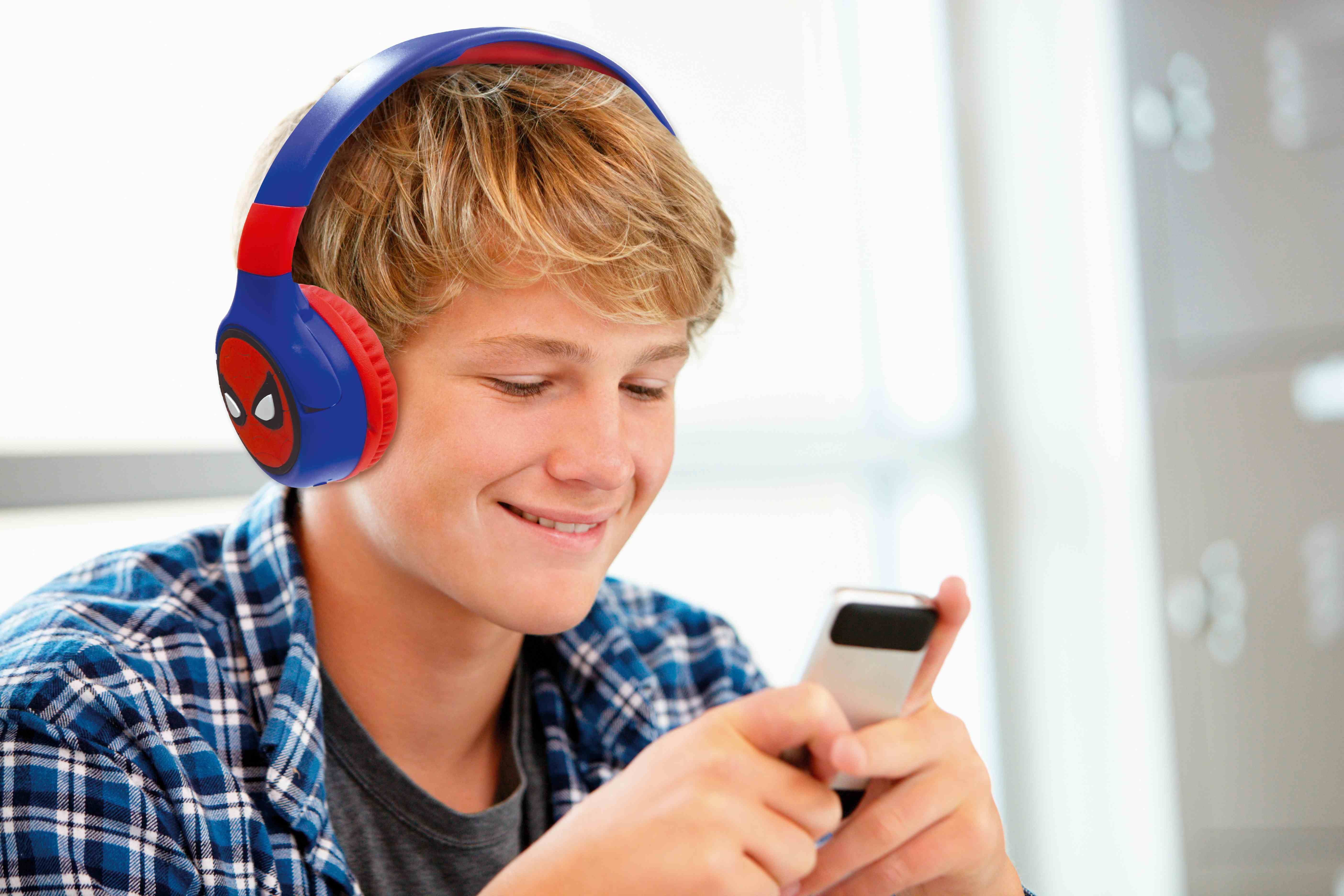 Młody mężczyzna w słuchawkach Spider-Man uśmiecha się, patrząc na telefon.