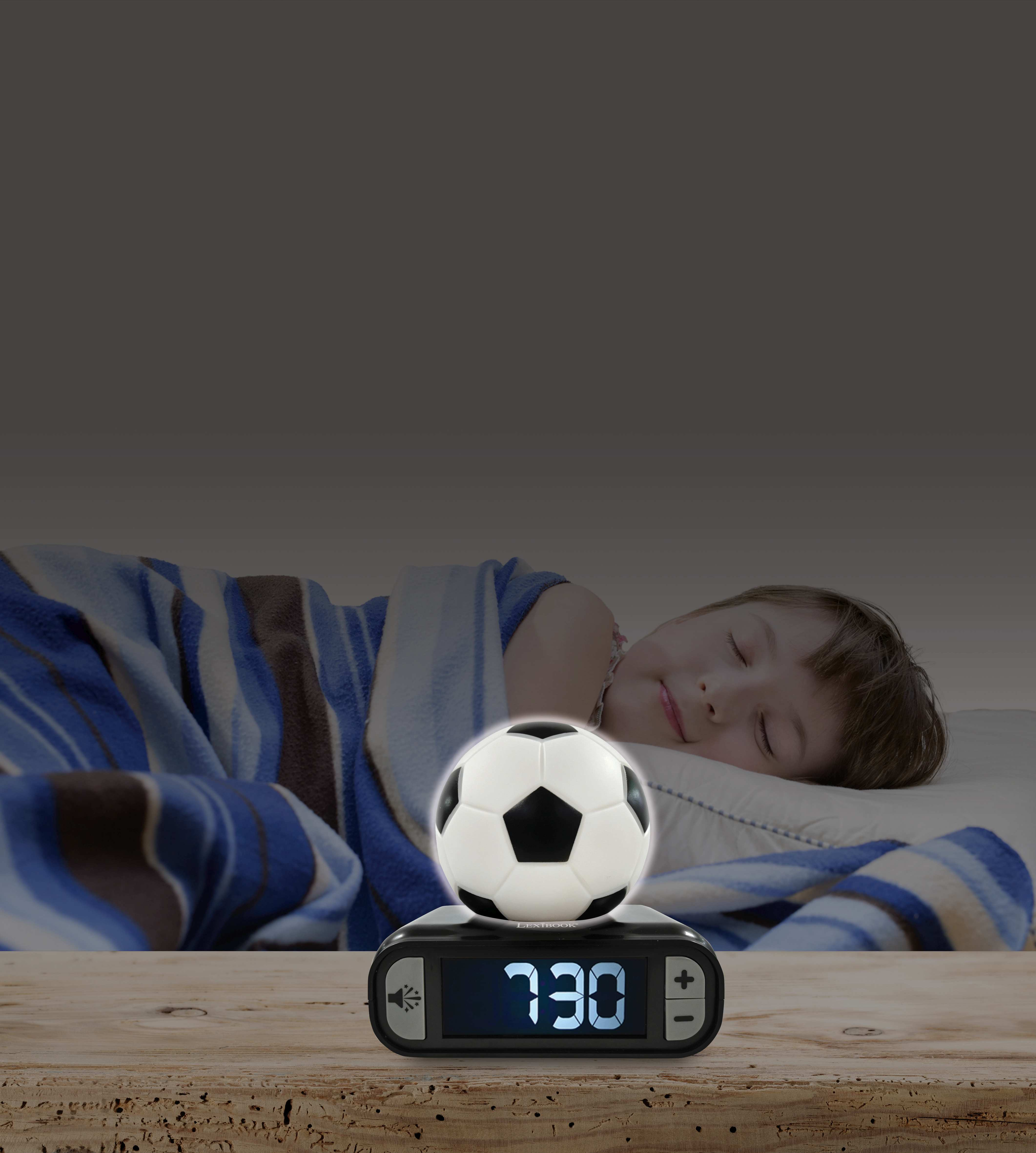 Un niño duerme en la cama mientras la hora 7:30 se muestra en un despertador con forma de balón de fútbol sobre una mesa de madera.