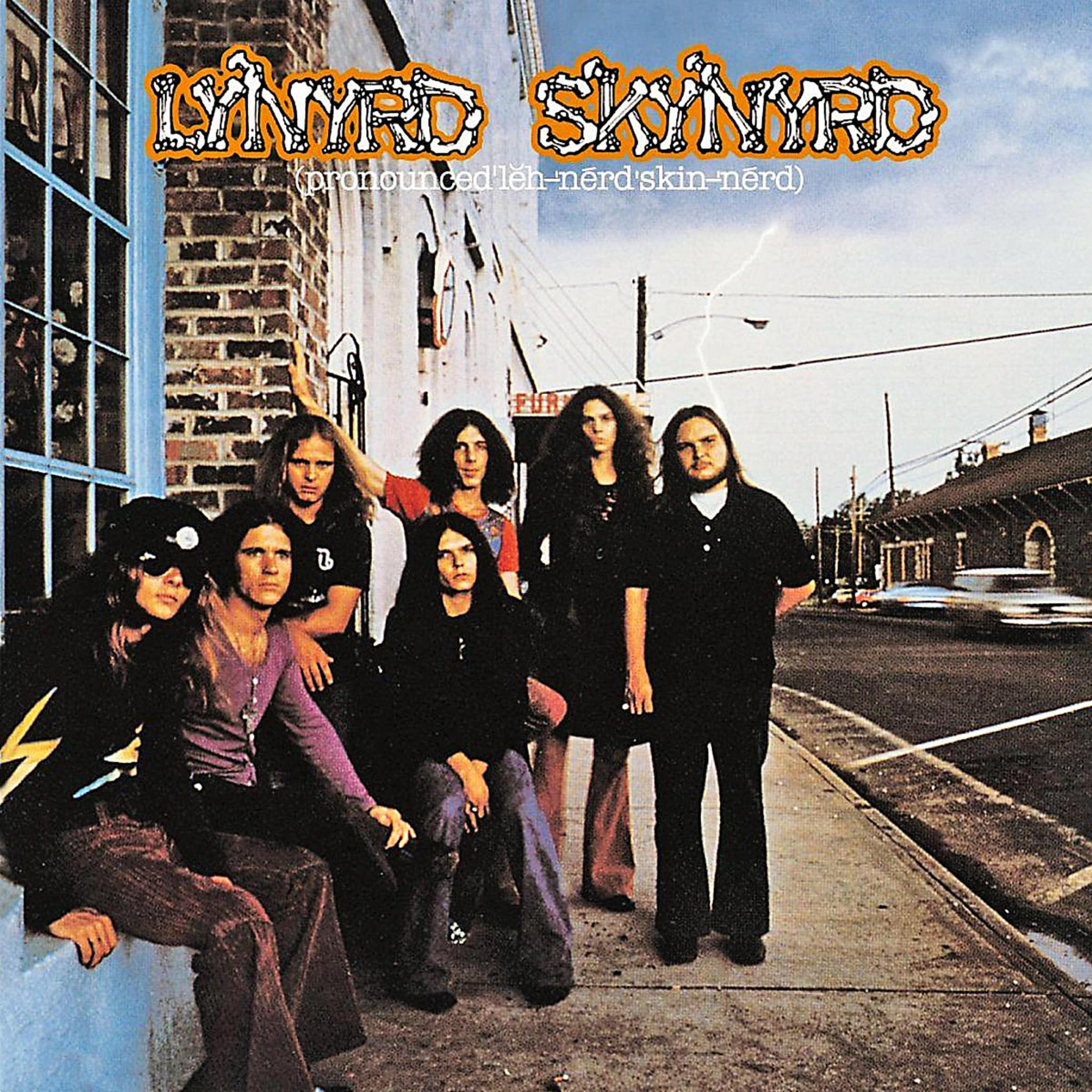 Portada del álbum Lynyrd Skynyrd, miembros de la banda en una acera, fondo de edificio antiguo.