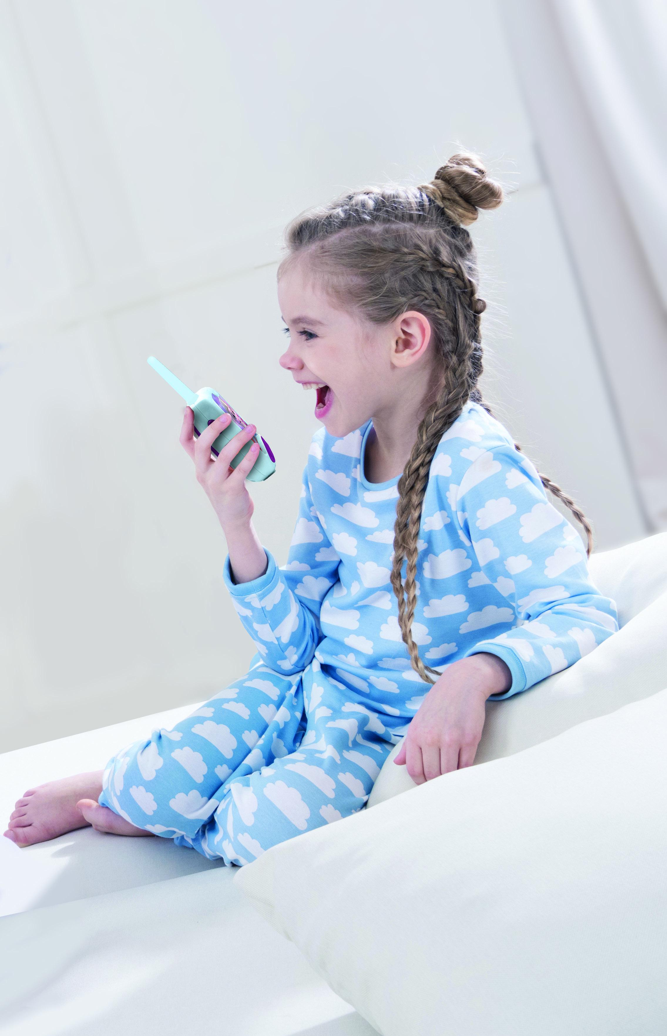 Dziewczynka w piżamie rozmawia przez walkie-talkie z Krainy Lodu, uśmiechając się na białej powierzchni.