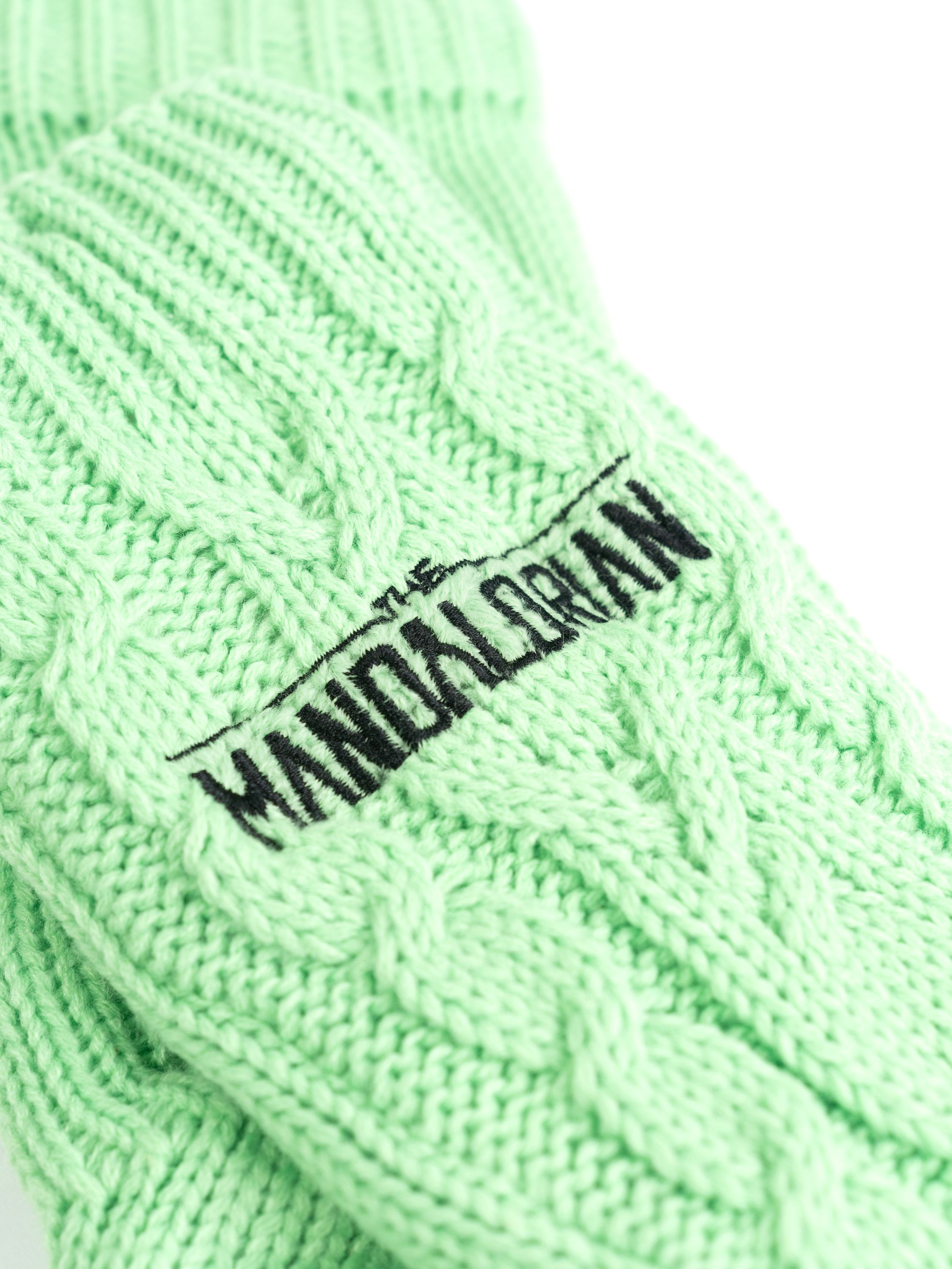 Nahaufnahme hellgrüner Strickhandschuhe mit schwarzer Stickerei "THE MANDALORIAN".