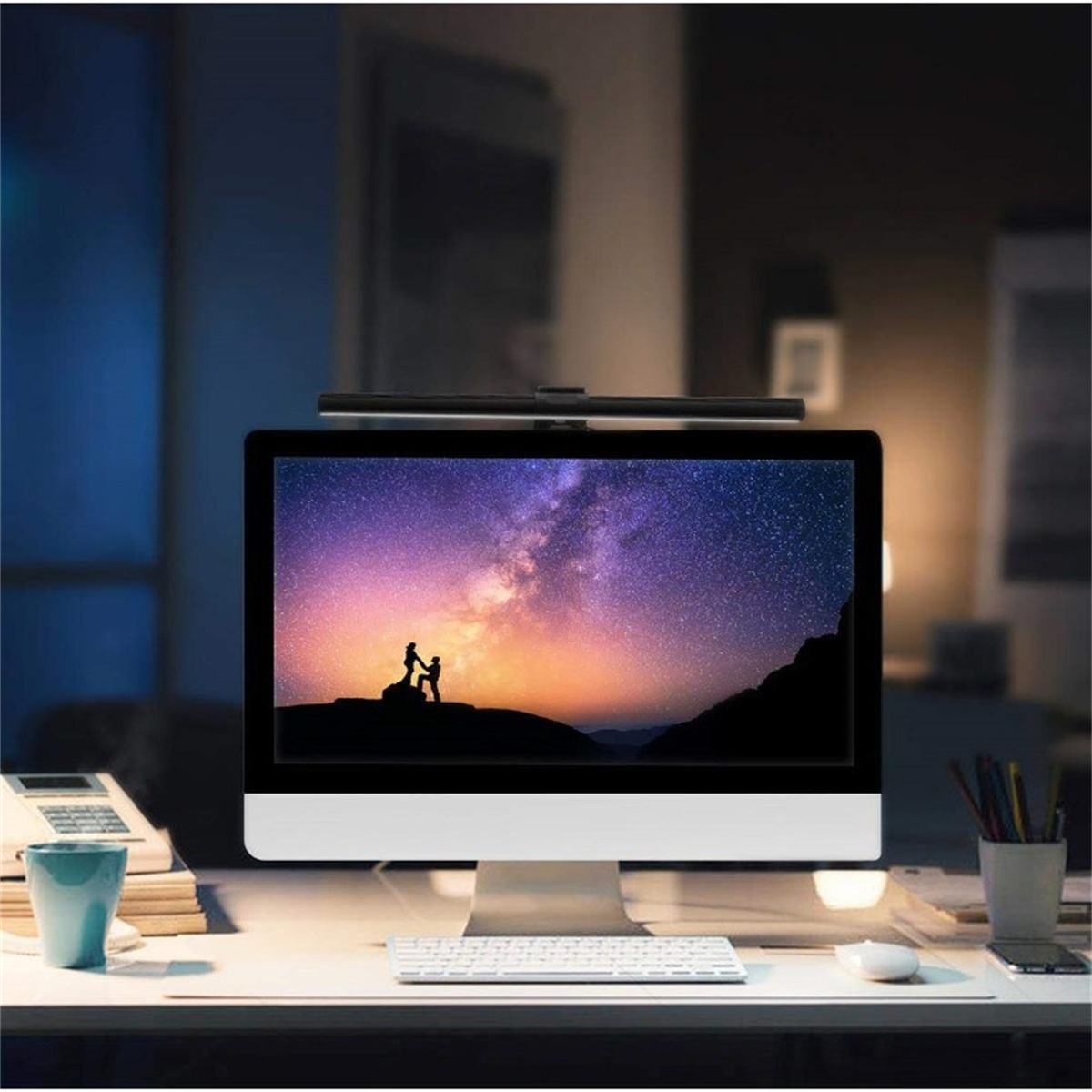 Ein Computermonitor, der einen Sternenhimmel mit zwei Figuren zeigt. Ein Schreibtisch, eine Tastatur und eine Lampe sind davor.