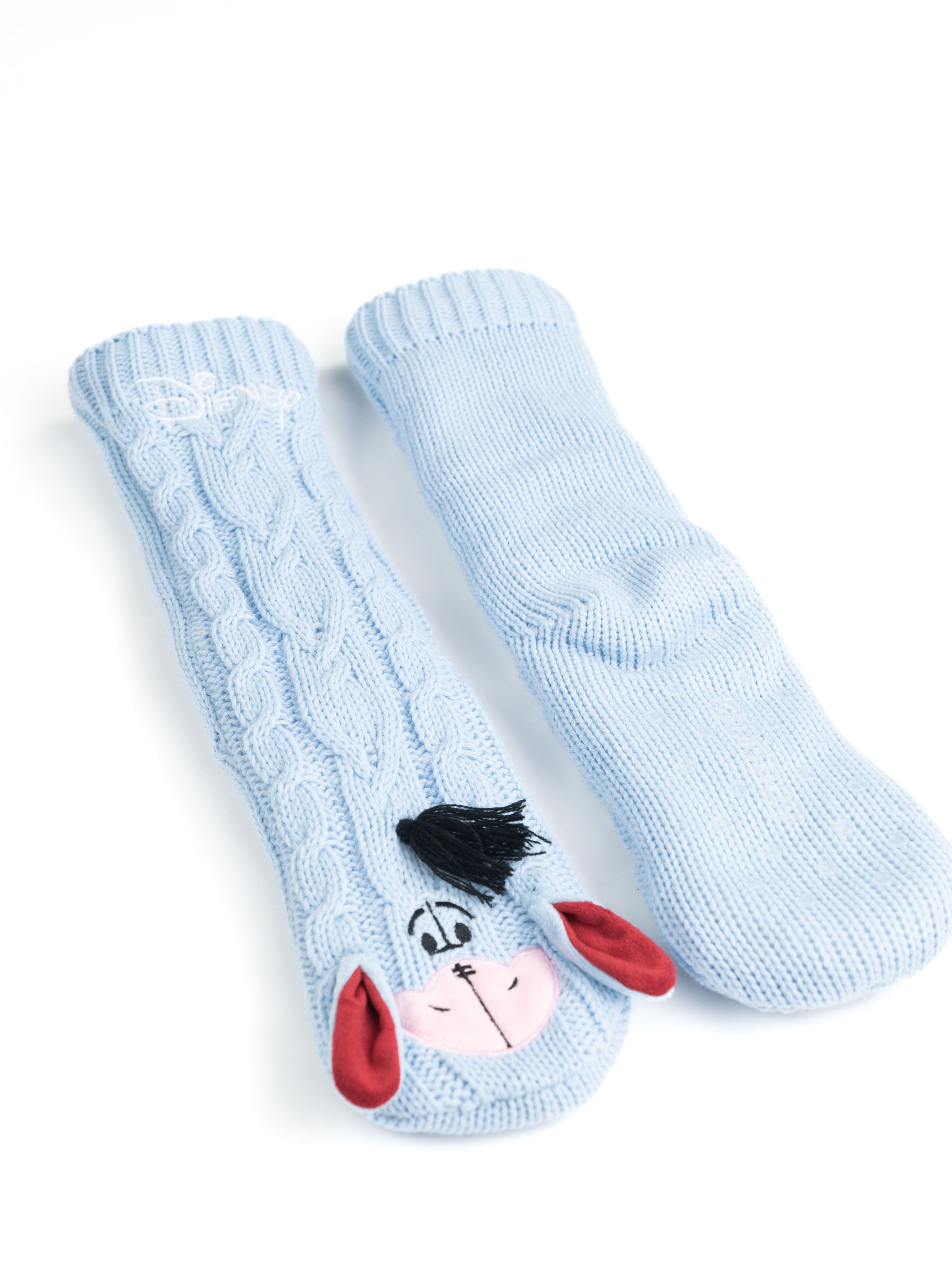 Zwei hellblaue Eeyore-Socken, eine mit Eeyores Gesicht und Disney-Logo, auf weißer Oberfläche.