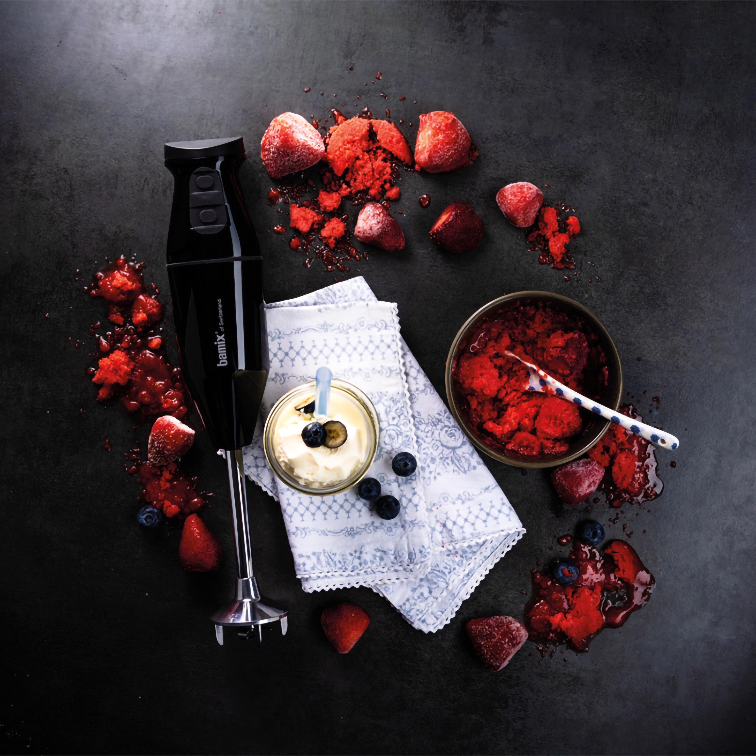 Frullatore a immersione nero con ingredienti per dessert: frutti di bosco, panna e una ciotola.