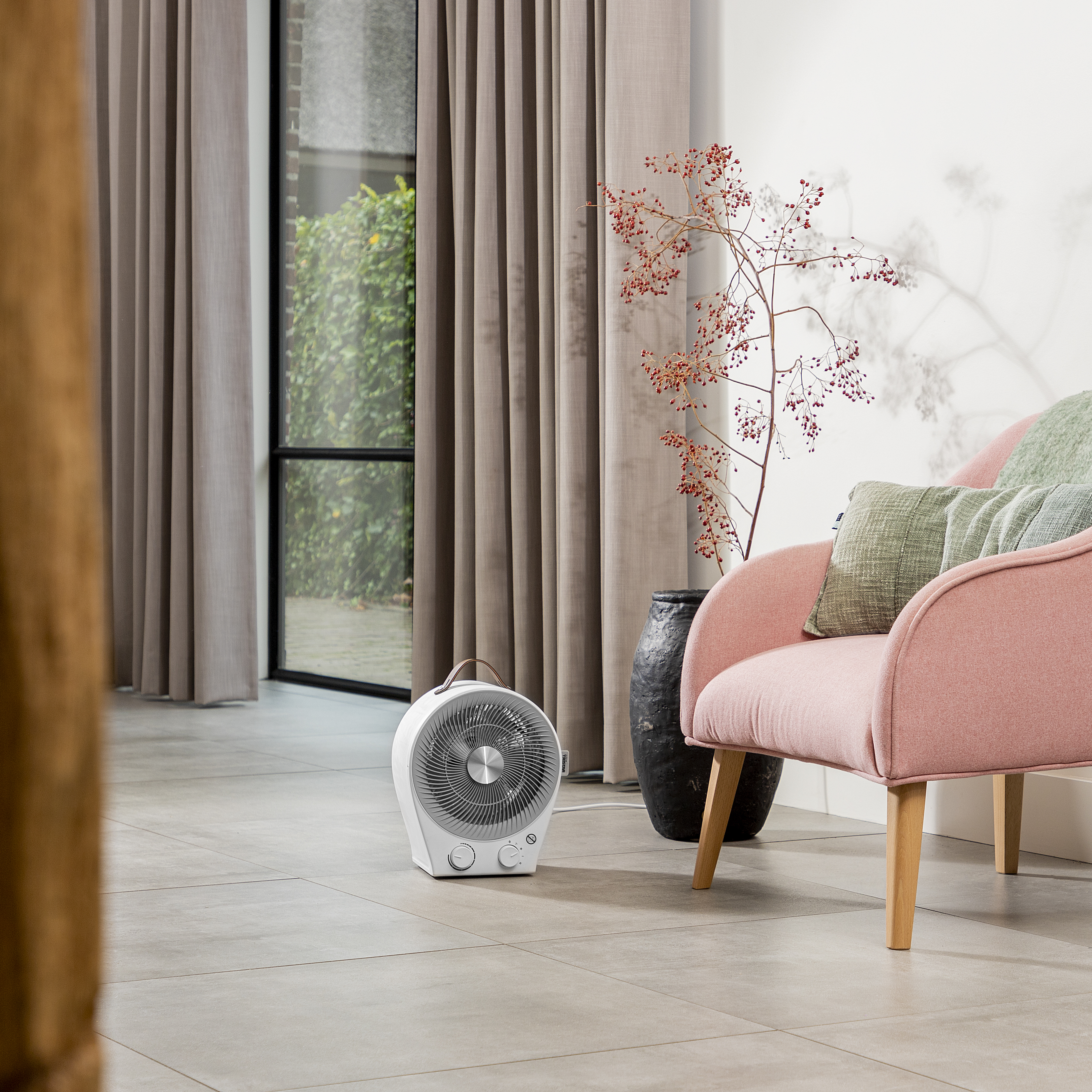 Salon z różowym fotelem, wentylatorem, zasłonami i roślinami. Szara podłoga z płytek. Światło naturalne.