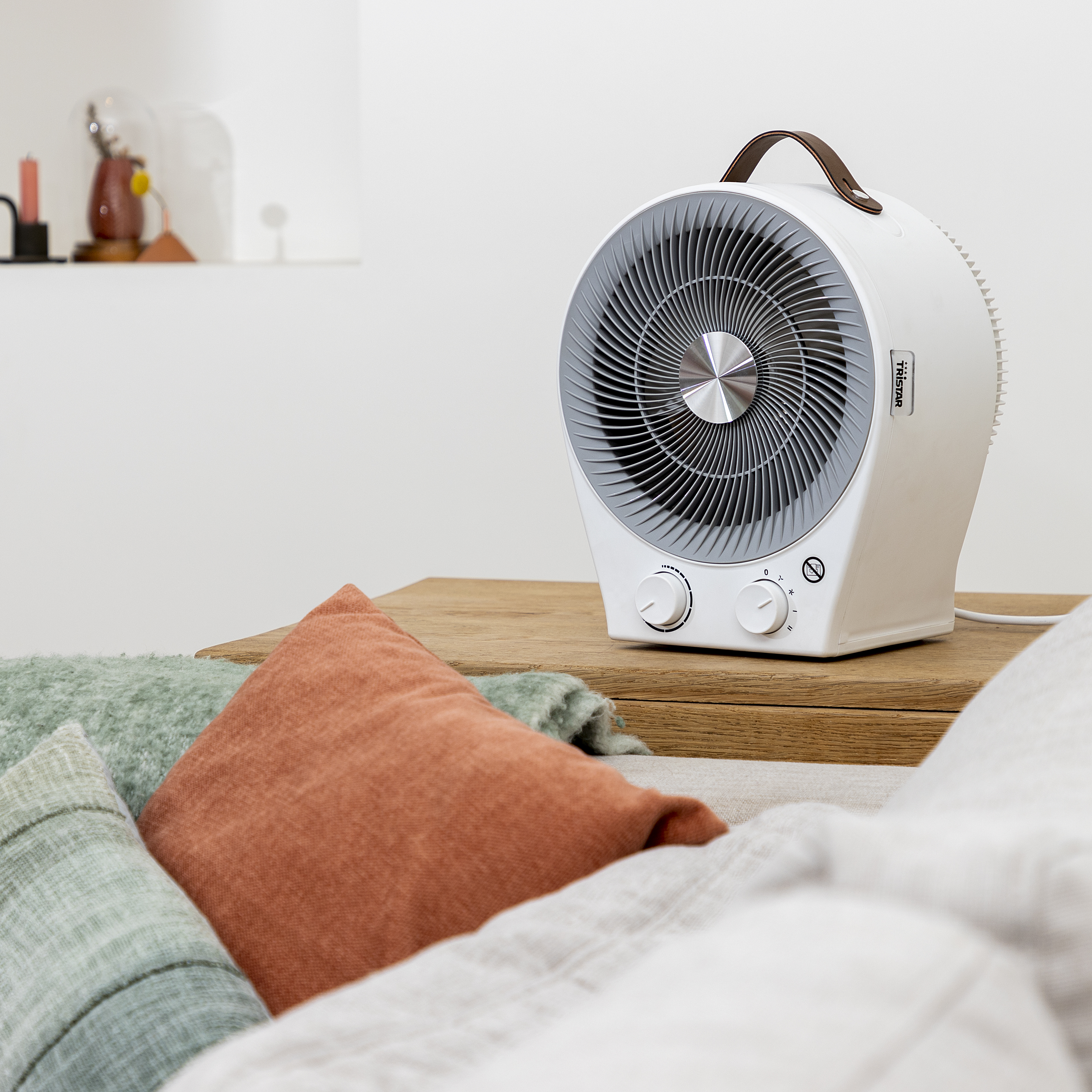 Biały wentylator na drewnianym stole z poduszkami i białym tłem.