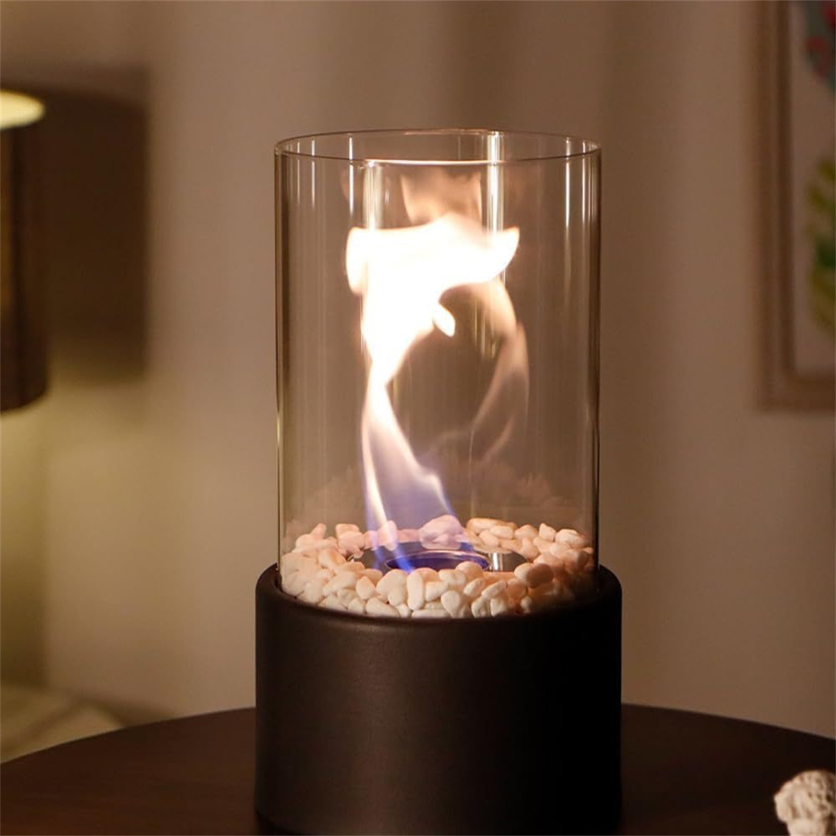 Kleiner Kamin mit Glaszylinder. Brennende Flamme mit weißen Steinen.