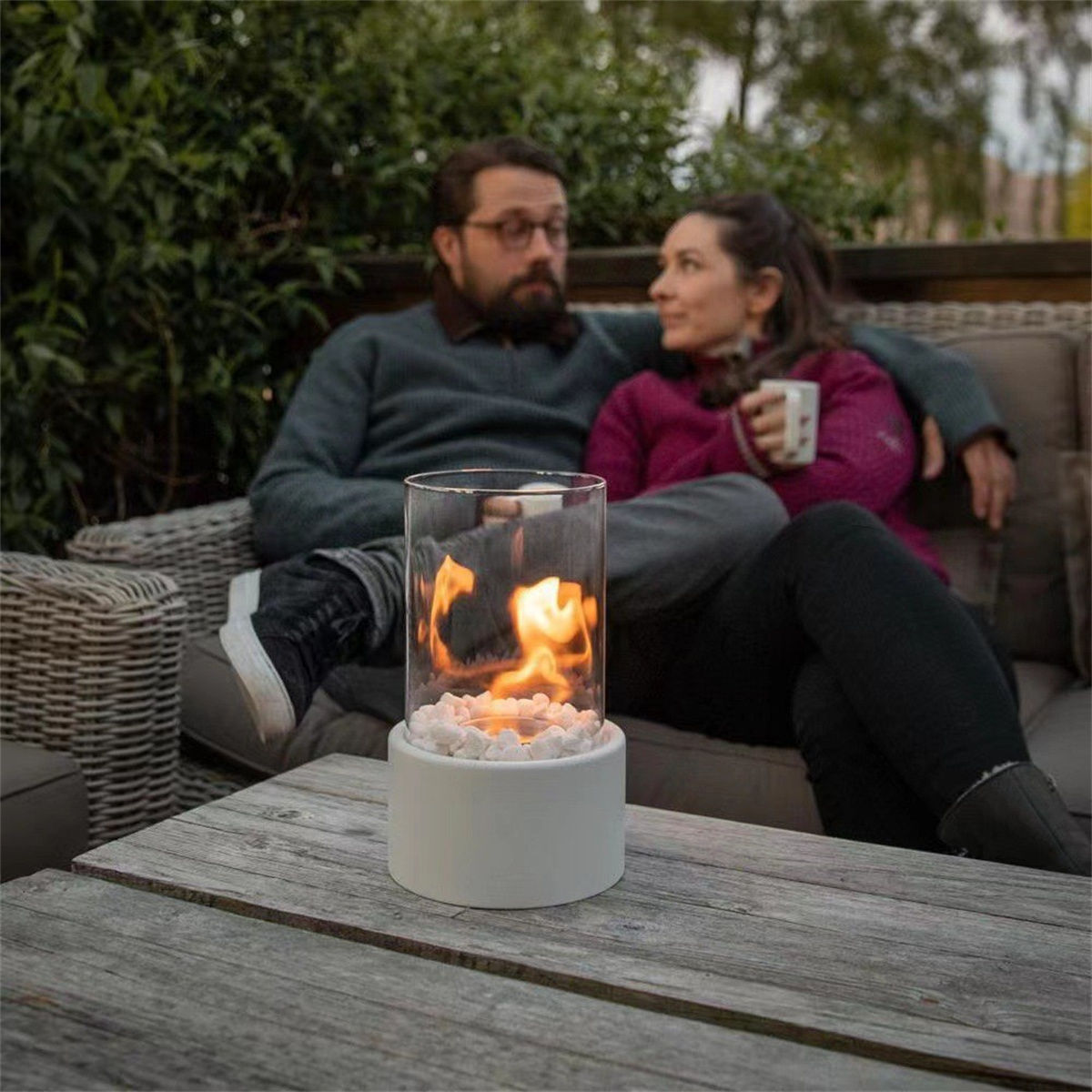 Paar auf einem Sofa an einem Tisch mit einem kleinen Feuerstelle. Die Feuerstelle enthält weiße Steine.