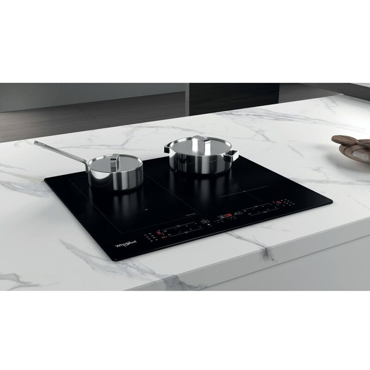 Encimera de inducción negra con dos ollas. Sobre encimera de mármol blanco. Marca Whirlpool visible.
