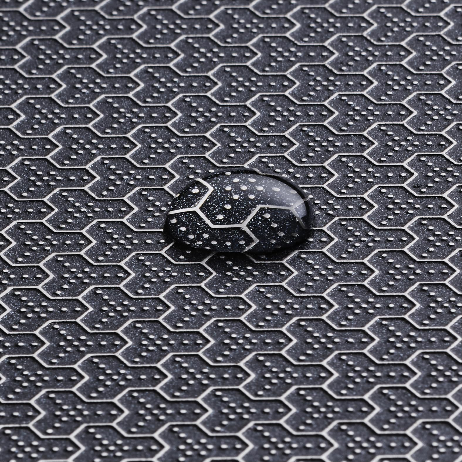 Ein Wassertropfen auf einer strukturierten hexagonalen Oberfläche, wodurch ein Muster aus Licht und Schatten entsteht.