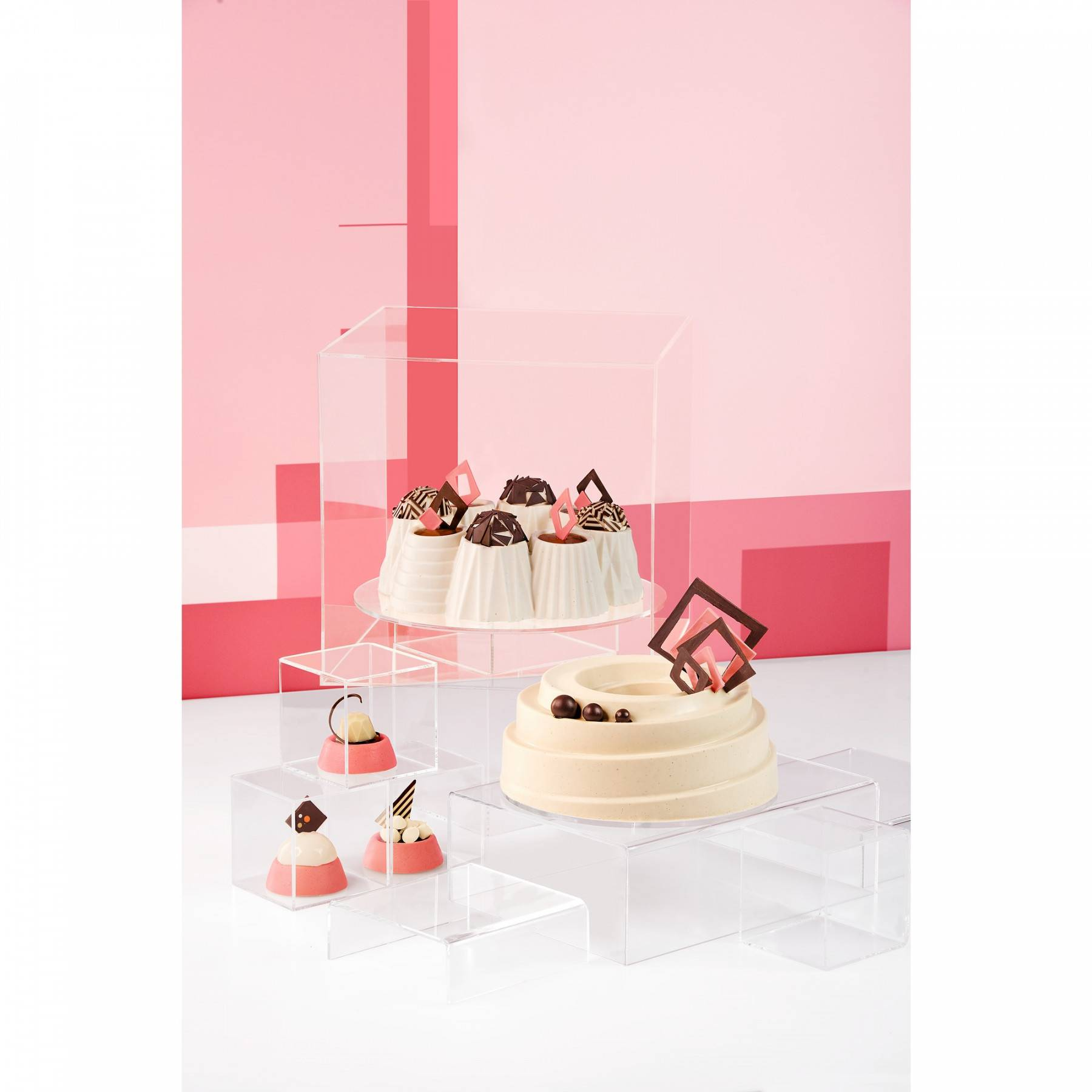 Kuchen auf transparenten Präsentationsständern. Einige sind auf einem weißen Kuchen. Rosa Hintergrund.