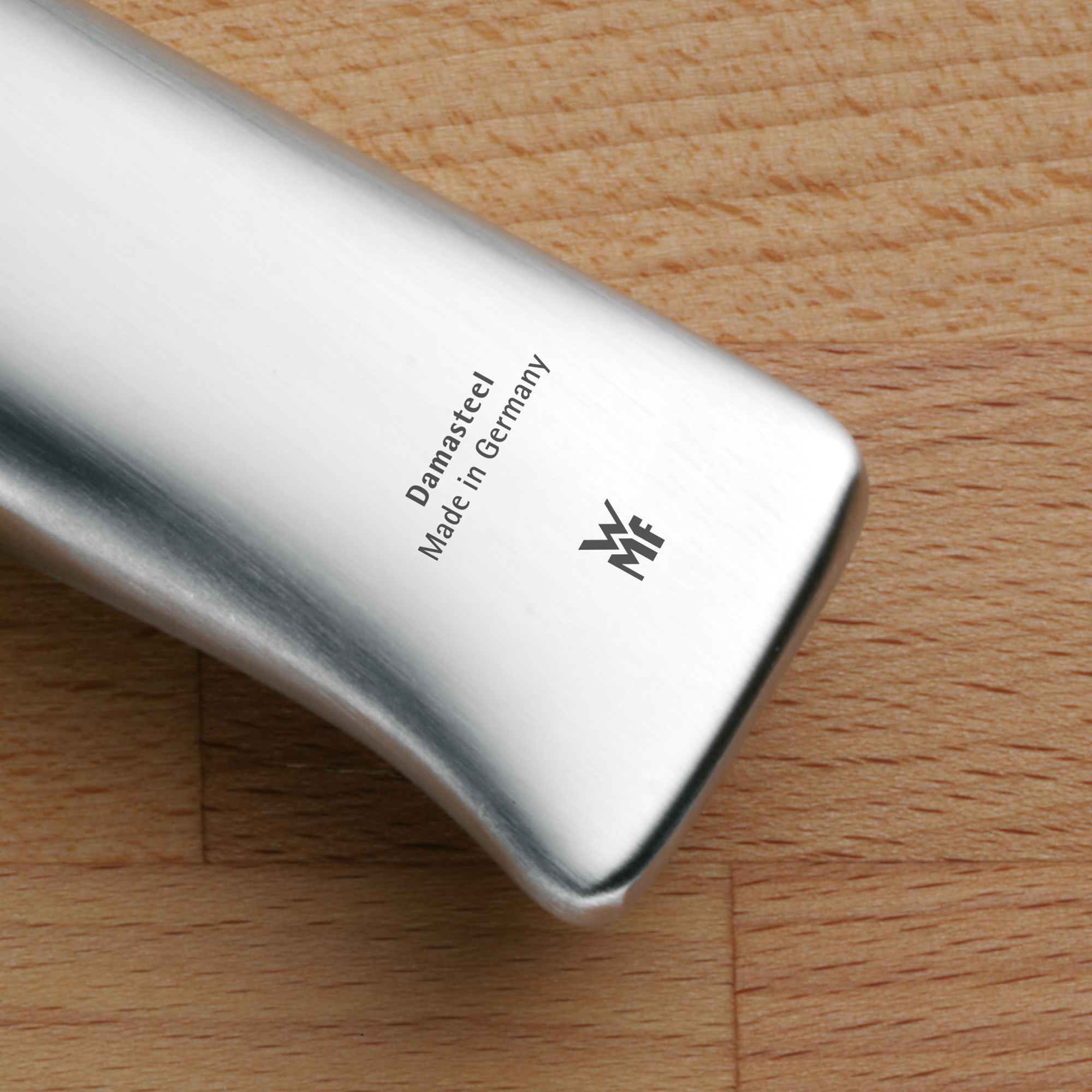 Zbliżenie ostrza noża z napisem 'Damasteel Made in Germany' i logo na drewnianej desce.