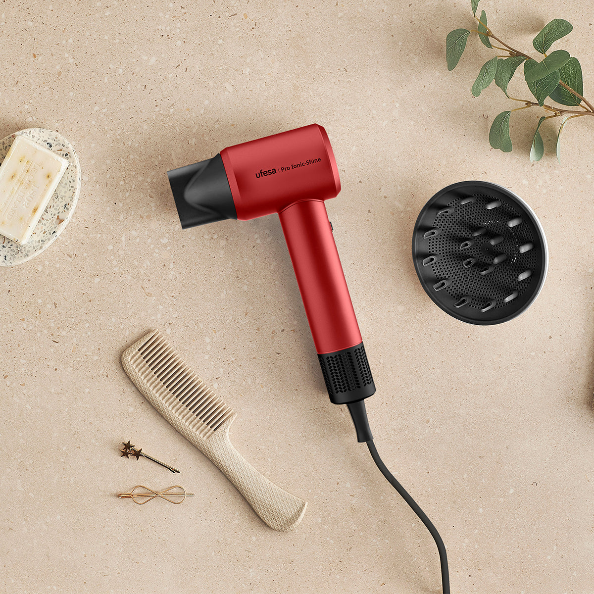 Czerwona suszarka do włosów z akcesoriami: grzebień, dyfuzor, spinki do włosów i mydło na beżowej powierzchni.