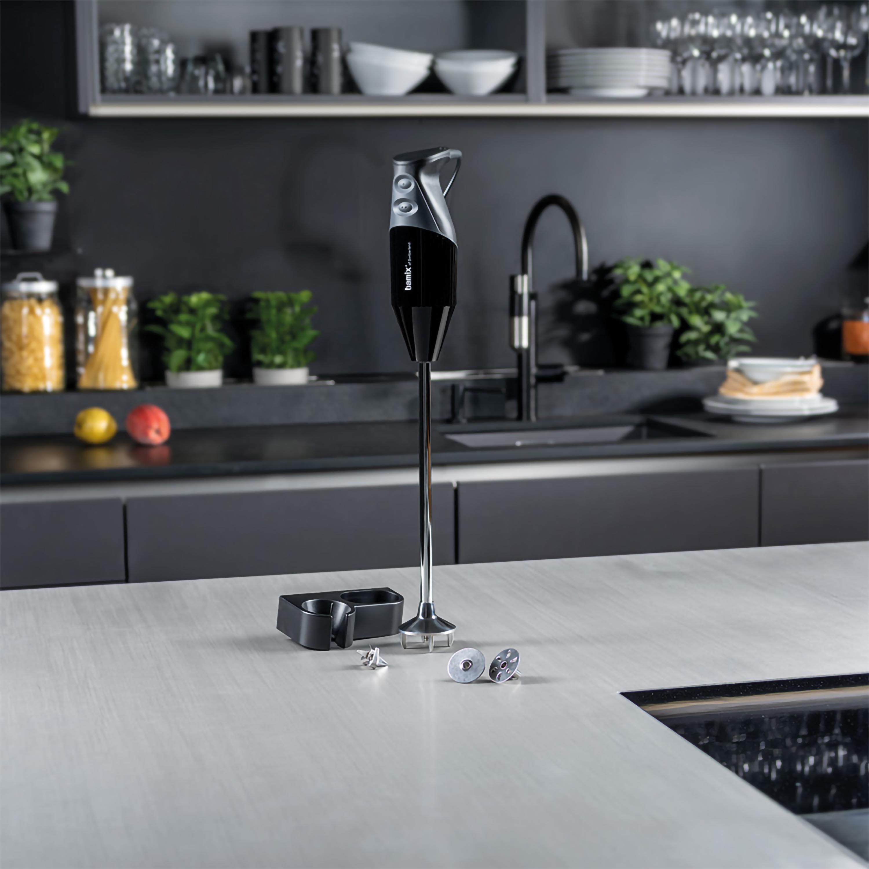 Frullatore a immersione nero con accessori su un piano cucina.