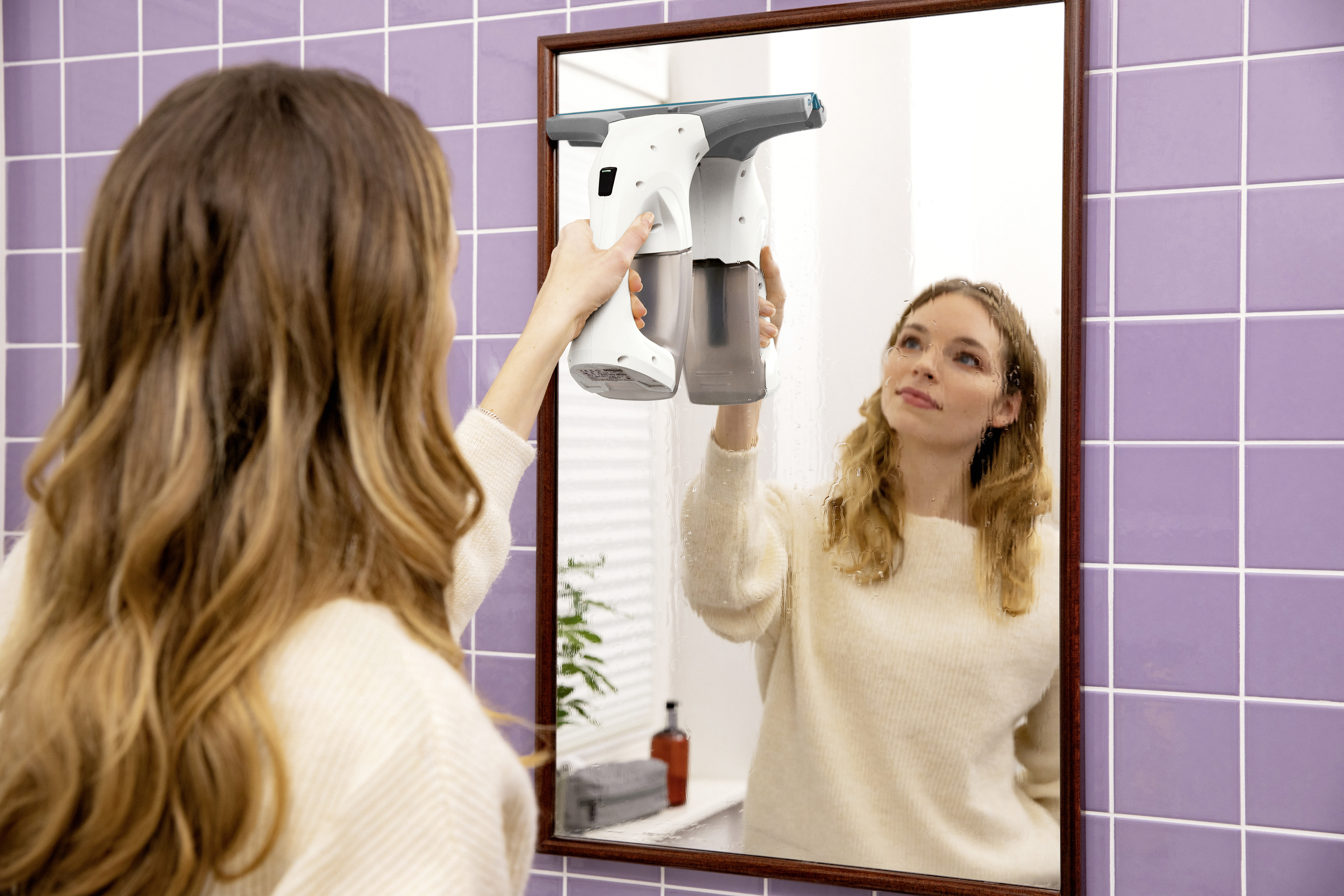 Femme nettoyant un miroir avec un appareil de nettoyage. Elle se regarde dans le miroir.