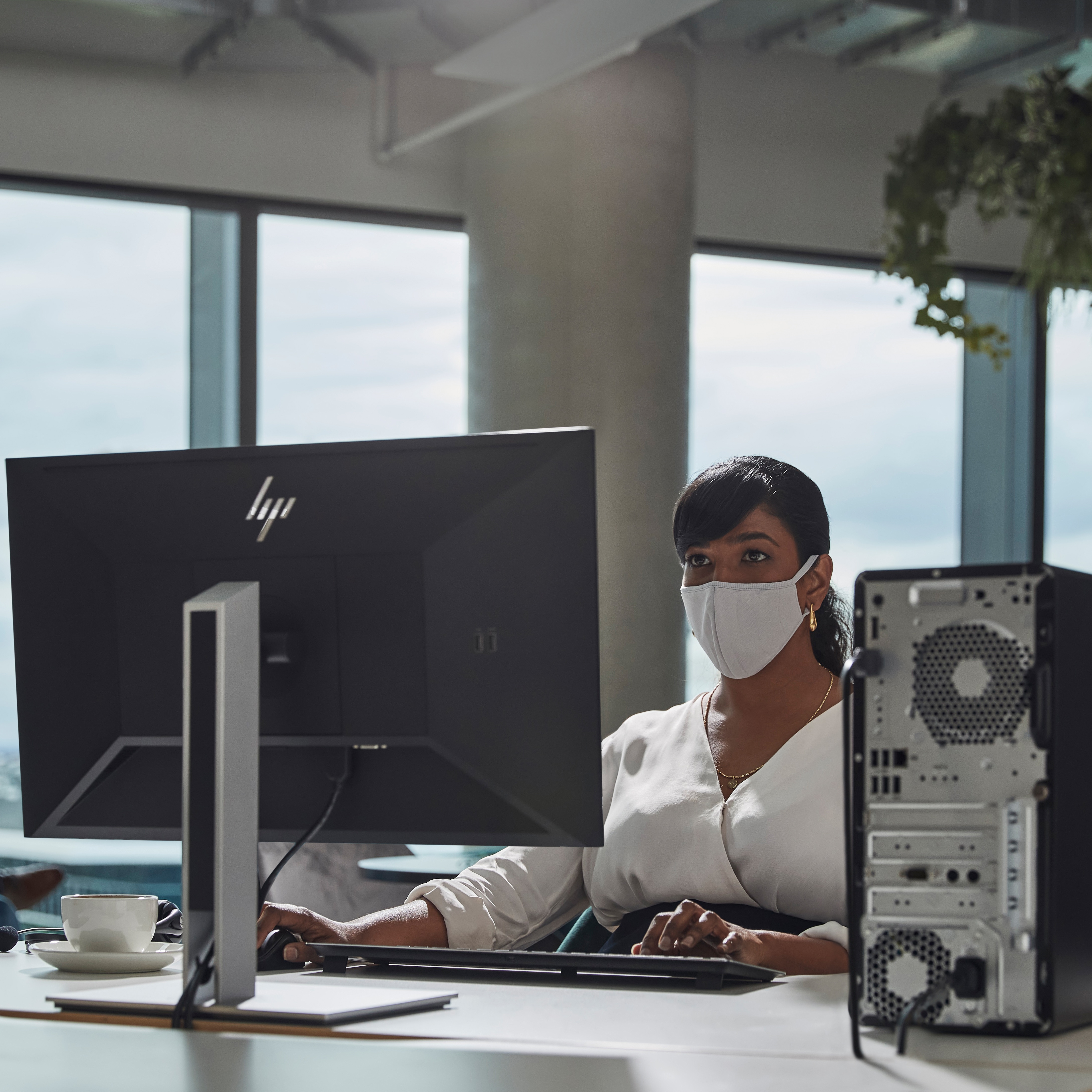 Kobieta w masce pracuje przy komputerze. Jest w biurze z oknem.