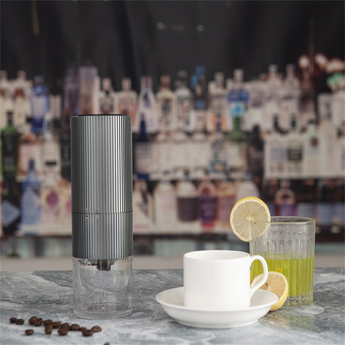 Eine Kaffeemühle, Kaffeebohnen, eine Tasse Kaffee und ein Glas Saft mit Zitronenscheiben. Barhintergrund.