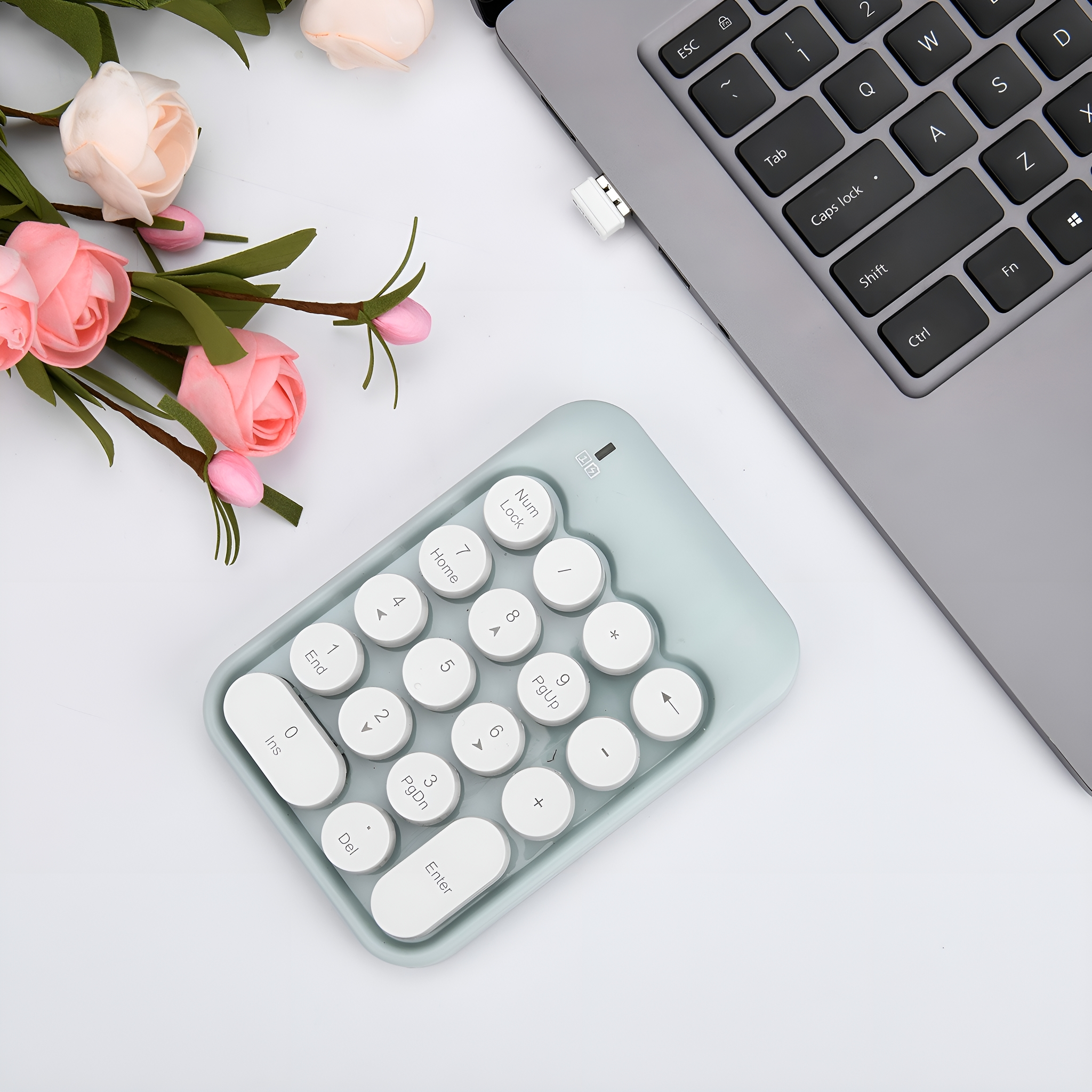 Numerischer Tastenblock neben einem Laptop mit Blumen auf weißem Hintergrund.