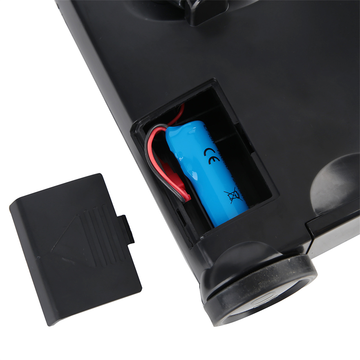 Ein Batteriefach an einem schwarzen Gerät. Eine blaue Batterie mit roten und schwarzen Drähten ist innen.