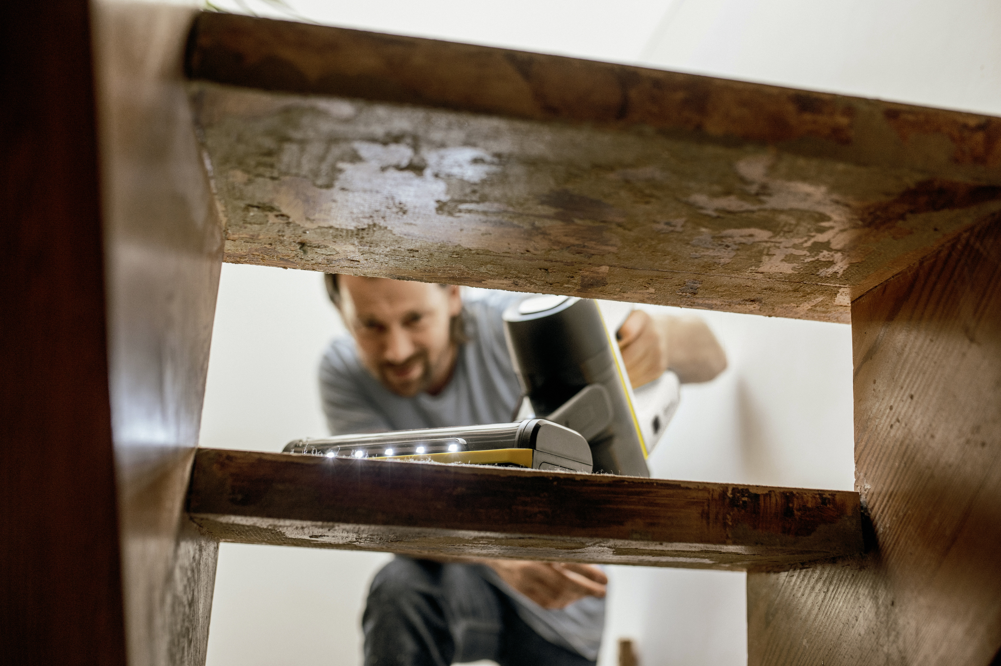 Homme utilisant un aspirateur sans fil sur des escaliers en bois, concentré sur le nettoyage.