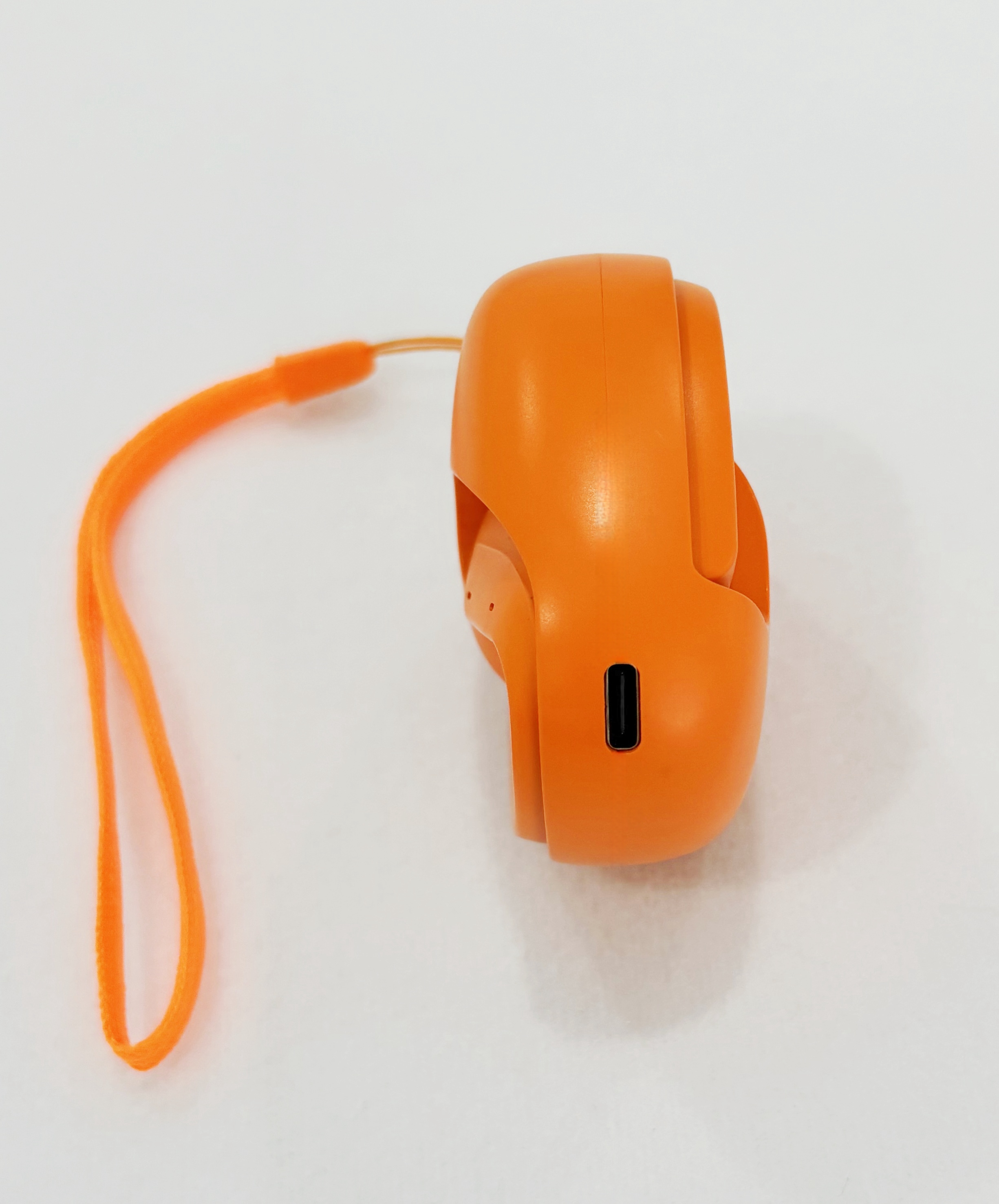 Altavoz portátil naranja. Correa naranja. Puerto negro. Fondo blanco.
