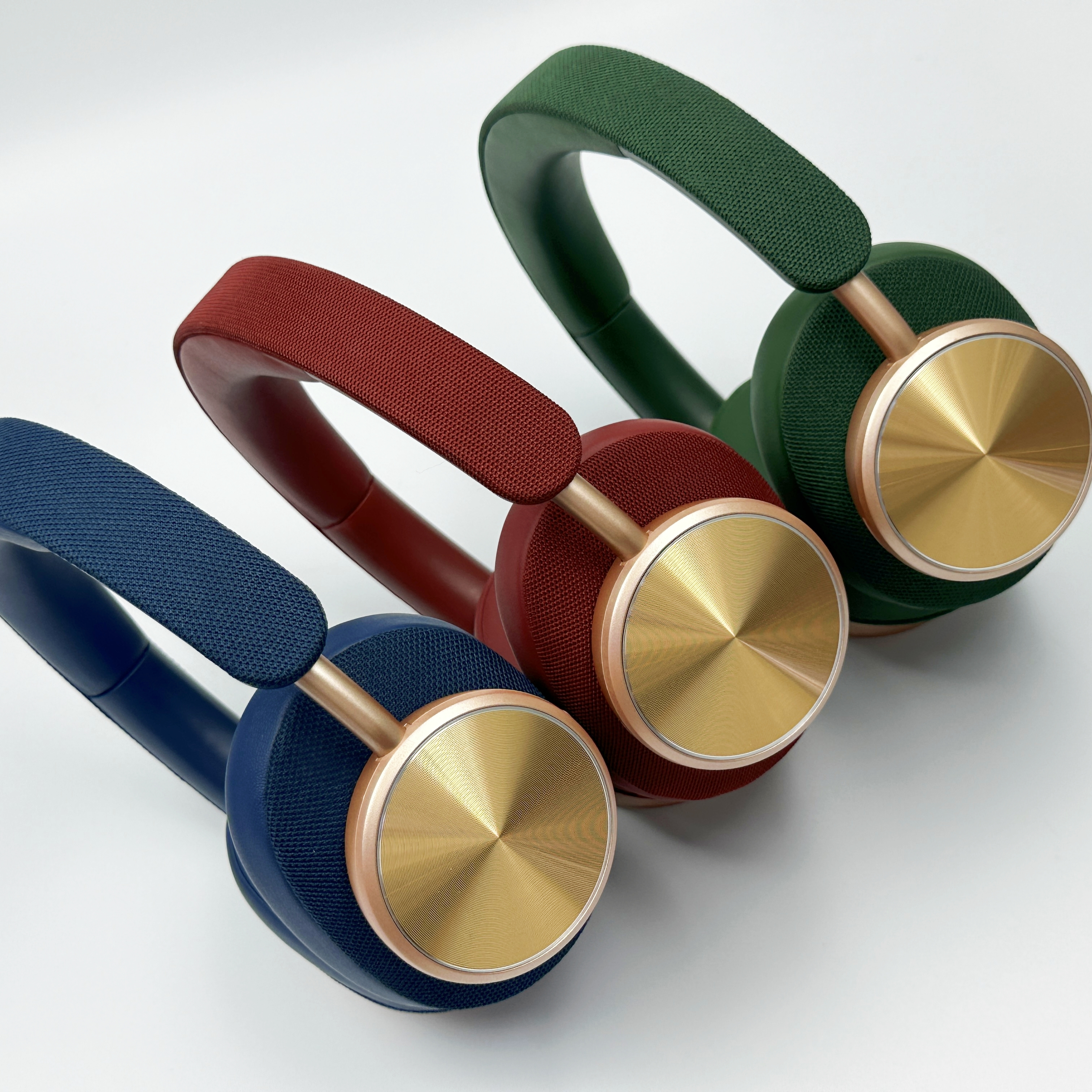 Tres pares de auriculares, azul, rojo y verde, copas doradas, fondo blanco.