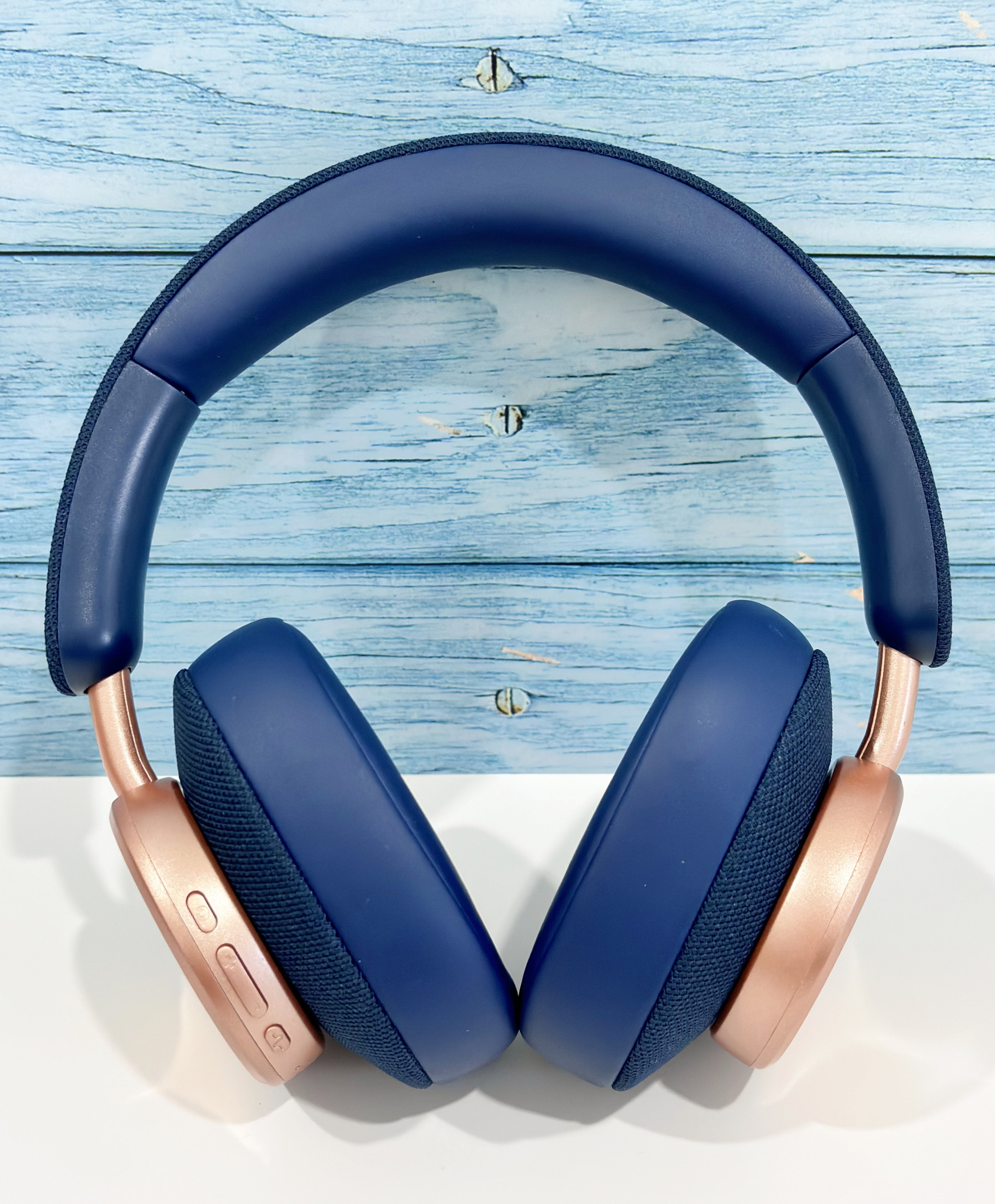 Auriculares circumaurales, azul marino con detalles en oro rosa. Colocados sobre una superficie de madera azul claro.