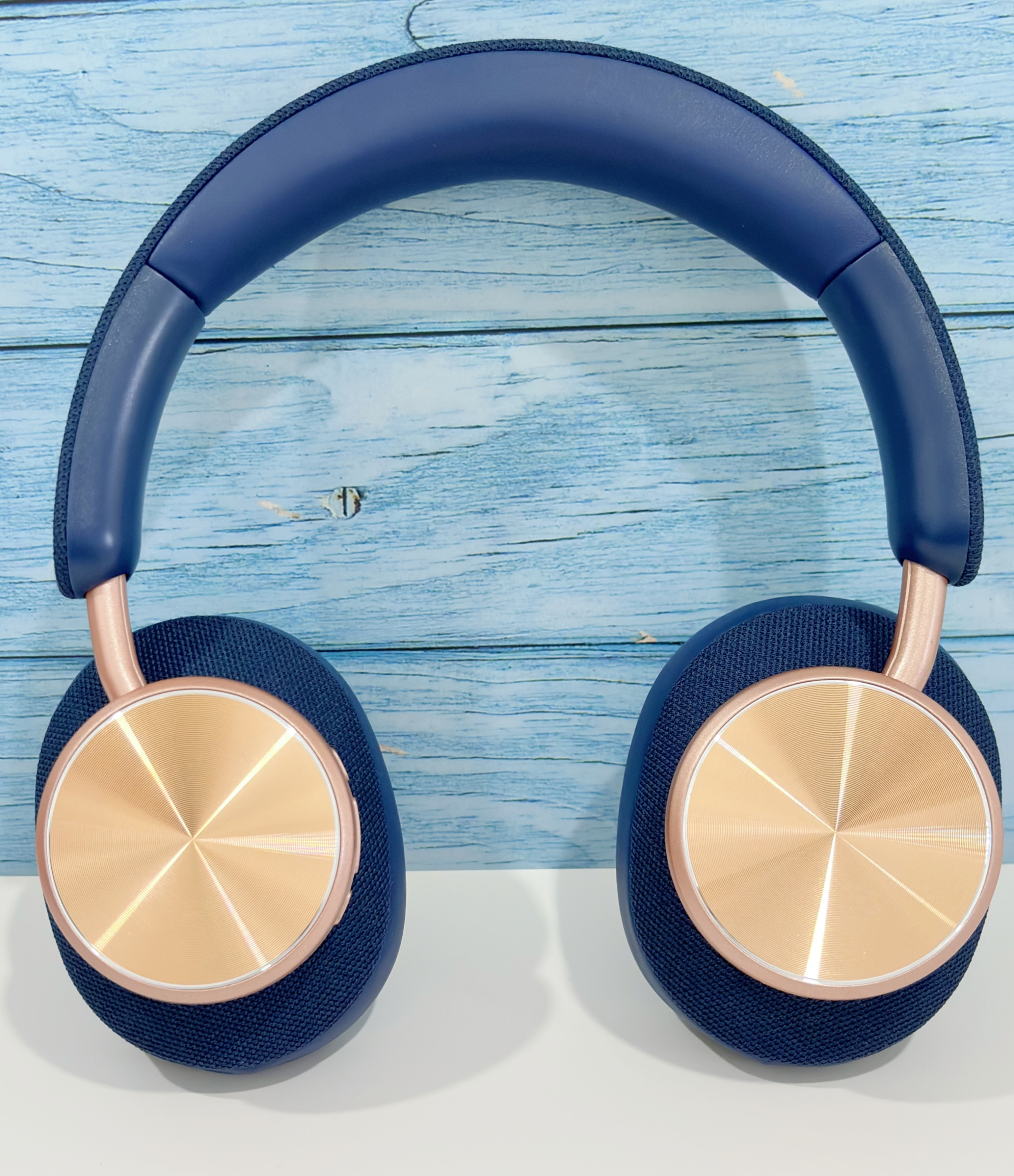 Auriculares azul marino con detalles en oro rosa y almohadillas circulares, sobre superficie blanca.